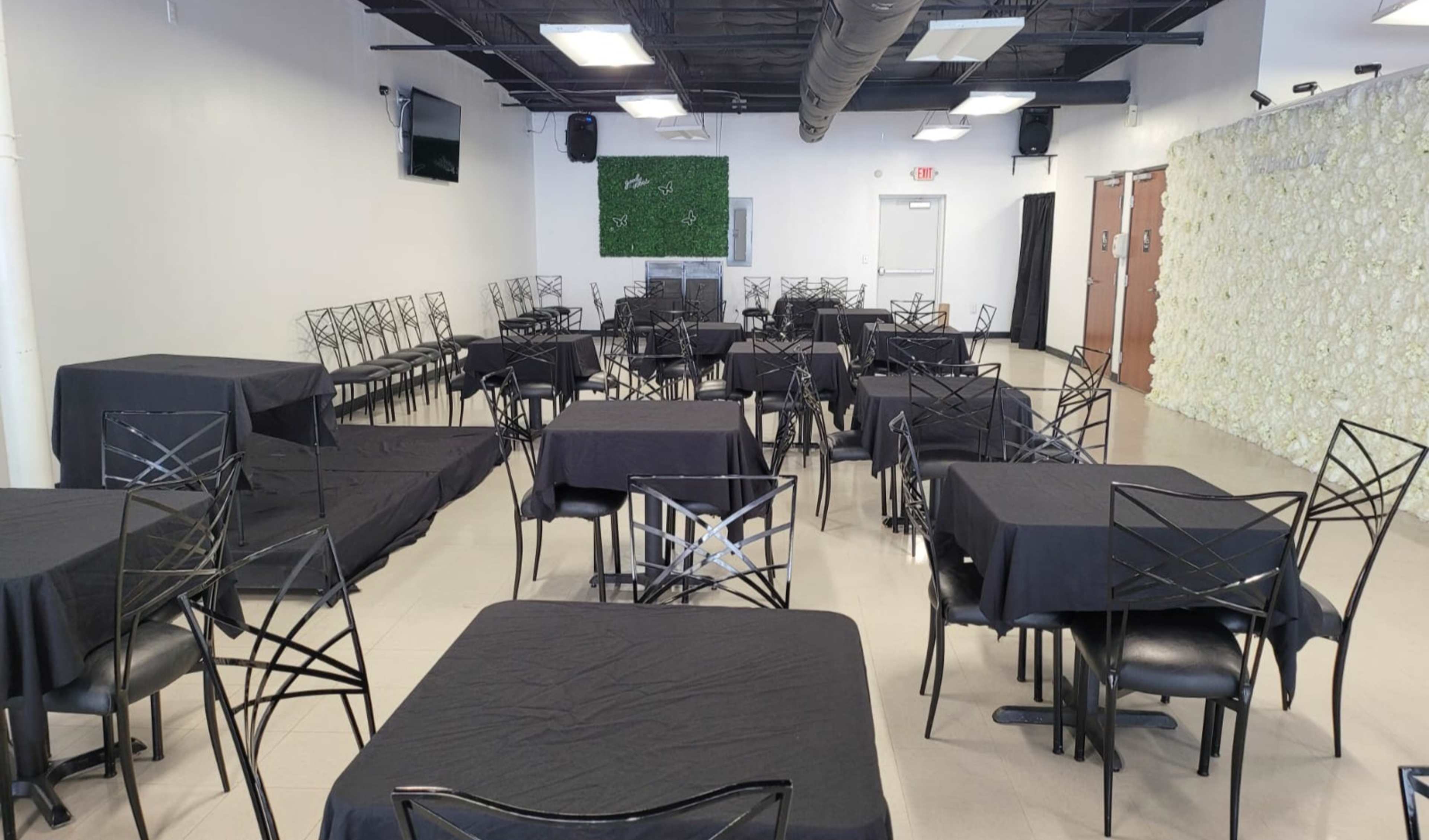 A spacious event venue set with multiple black-covered tables arranged in a grid layout.
