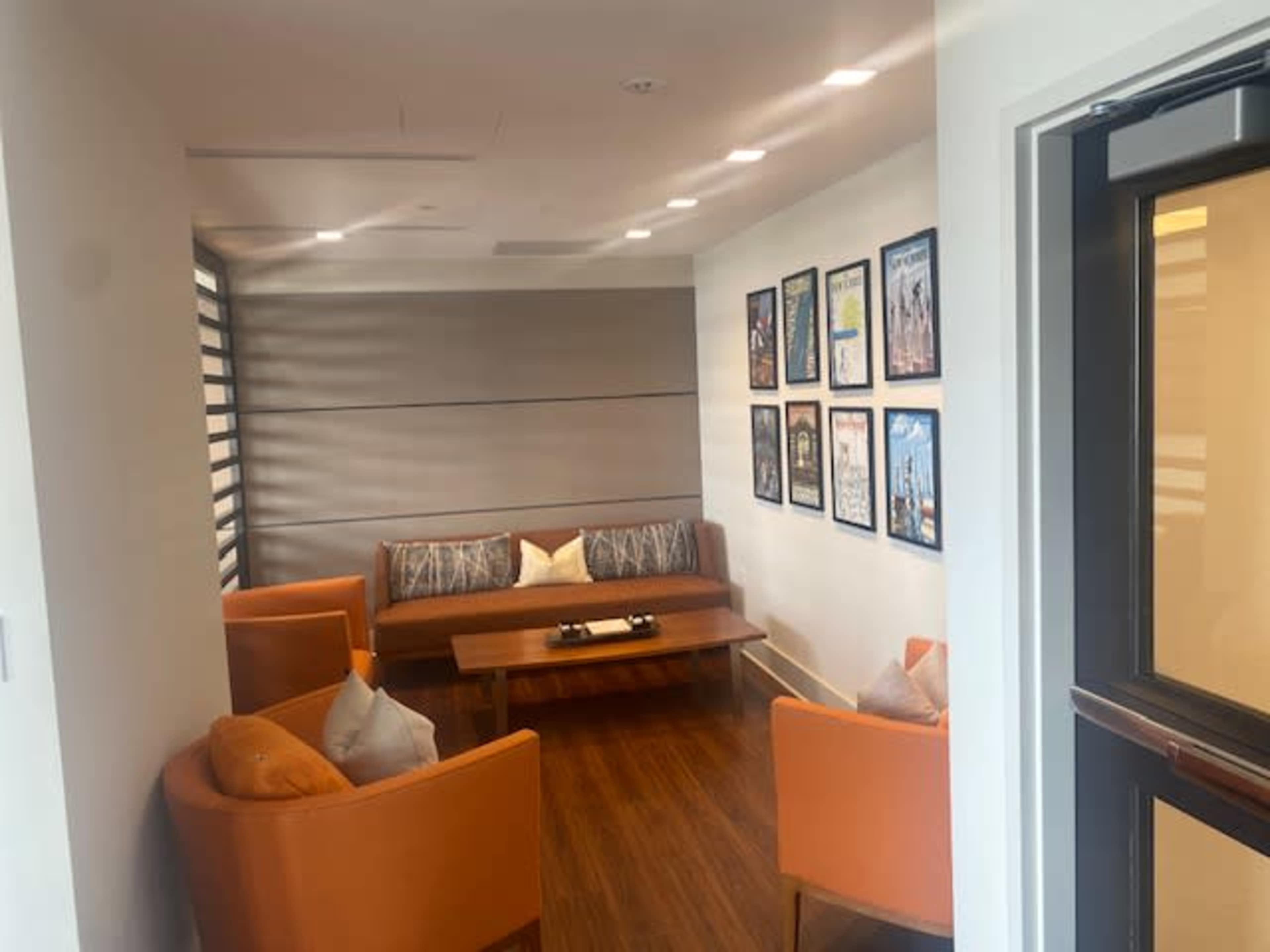 A small lounge area furnished with orange chairs, a wooden coffee table, and a sofa, accompanied by framed artwork on the wall.