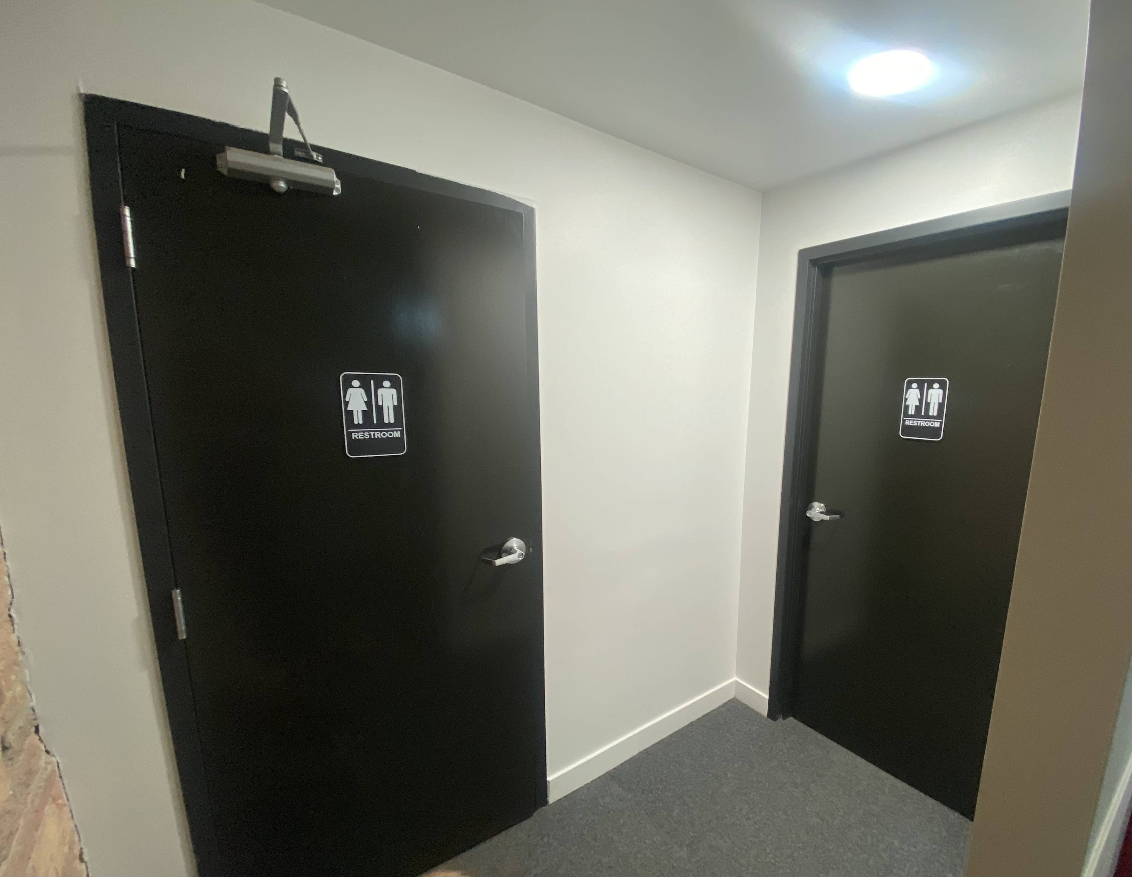 A hallway with two black restroom doors, one labeled "Men's Room" and the other labeled "Women's Room."