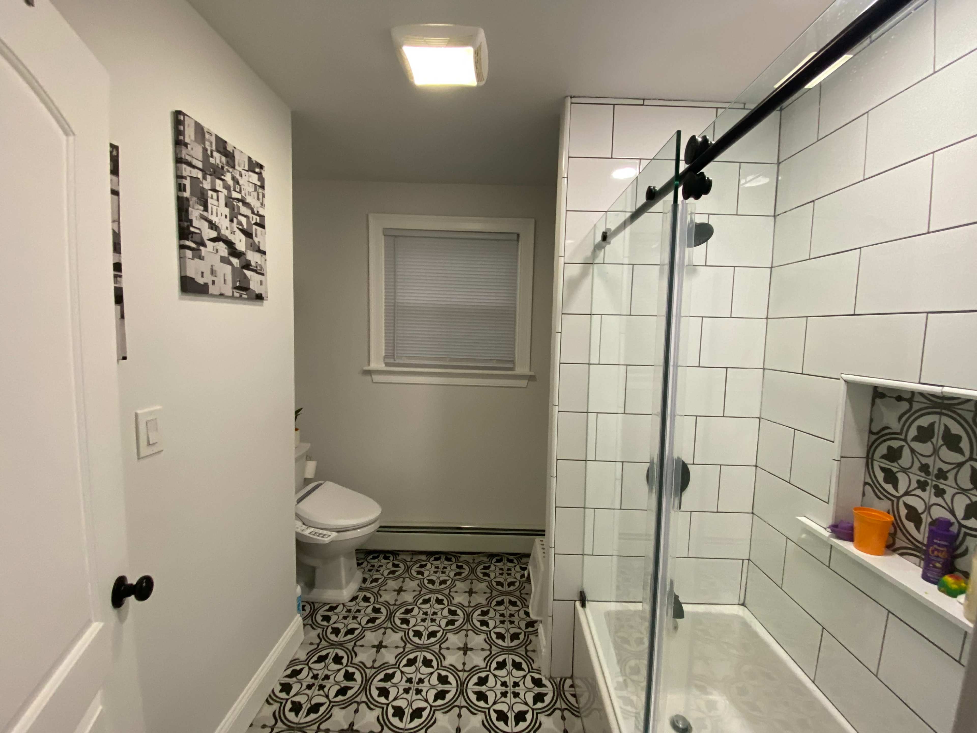 A bathroom with a glass shower, tiled walls, and a patterned floor.