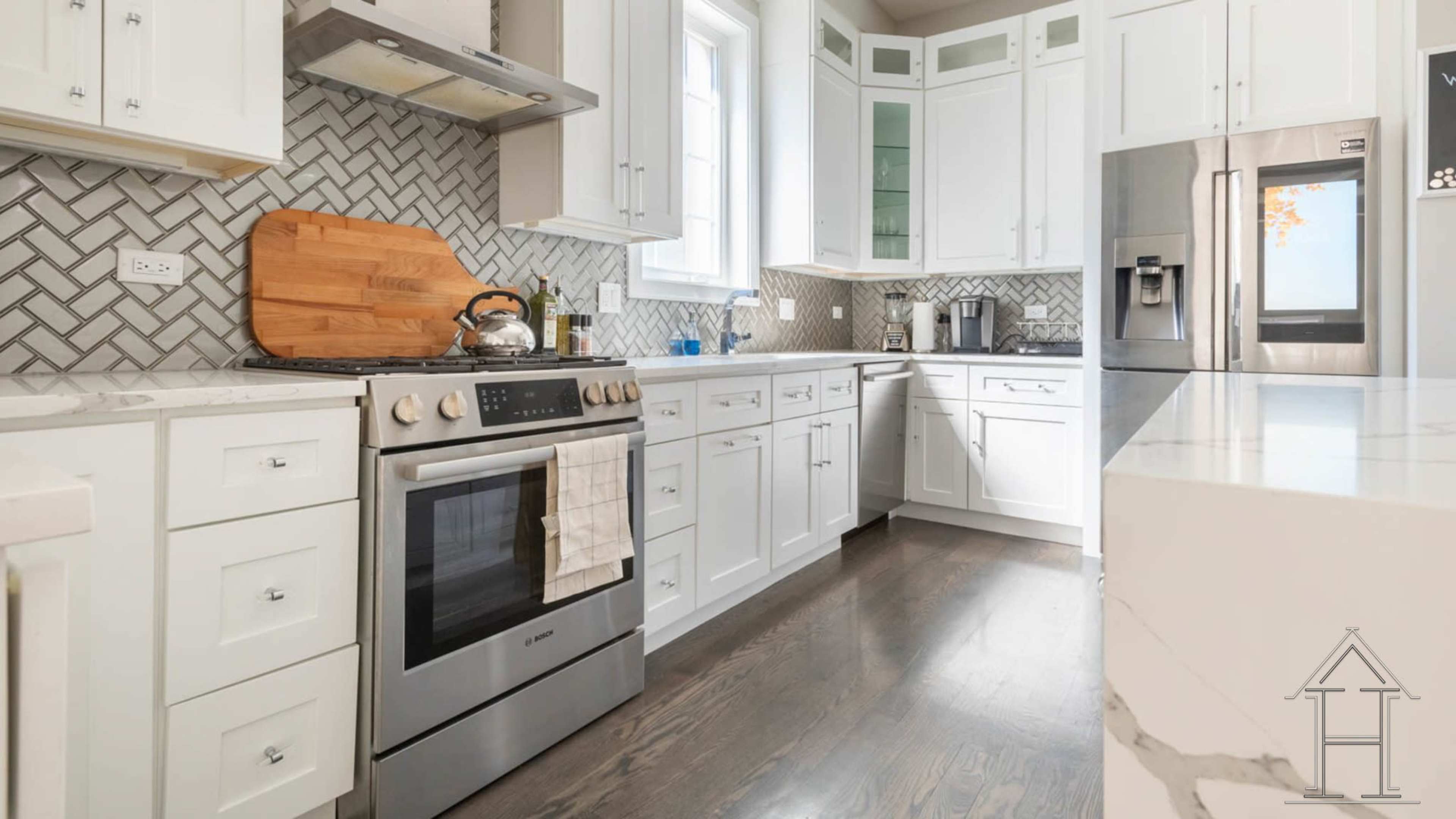 A modern kitchen features white cabinetry, a stainless steel stove with an organized countertop, and a herringbone tiled backsplash.