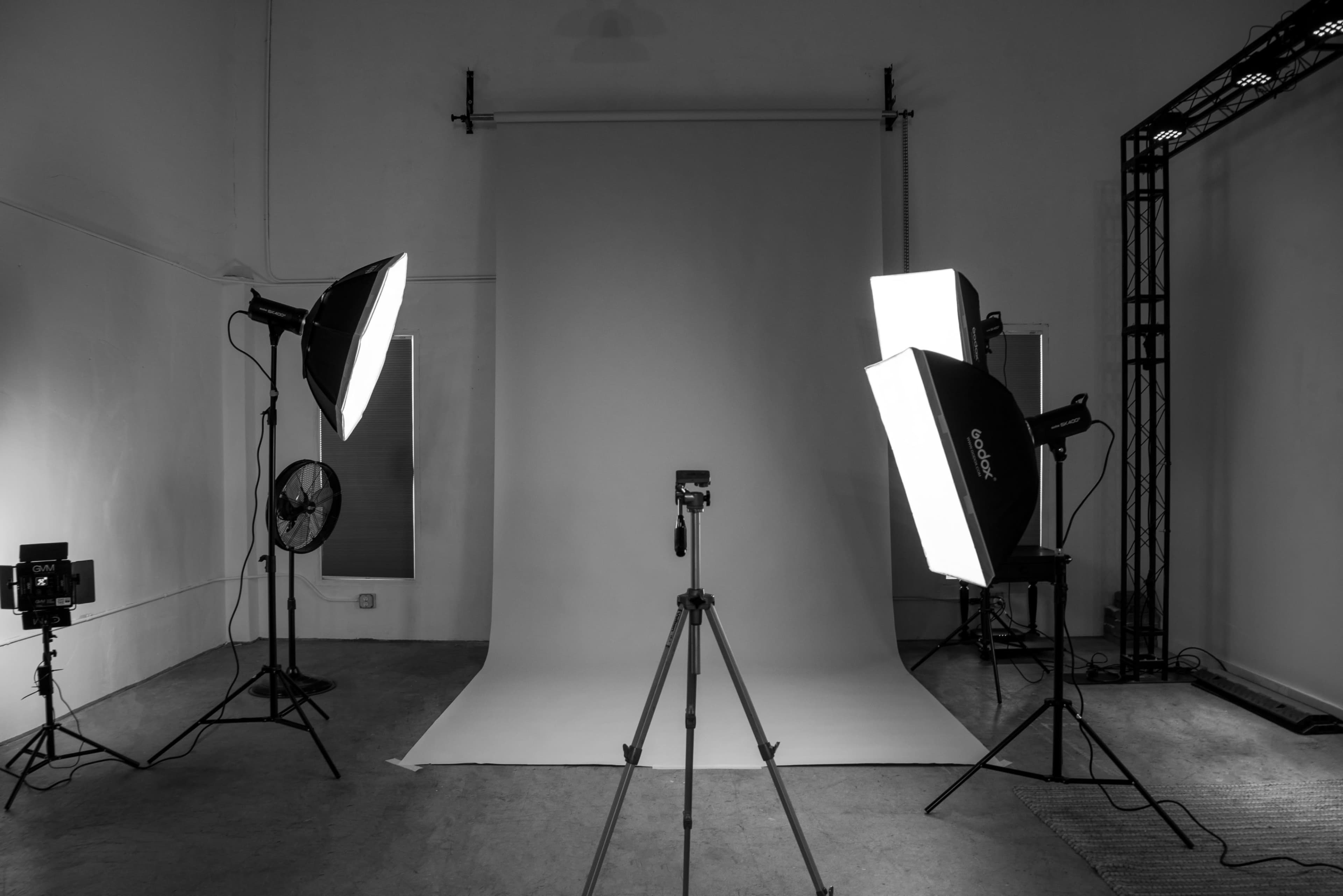 A photography studio is set up with a backdrop, two softbox lights, a tripod, and additional lighting equipment.