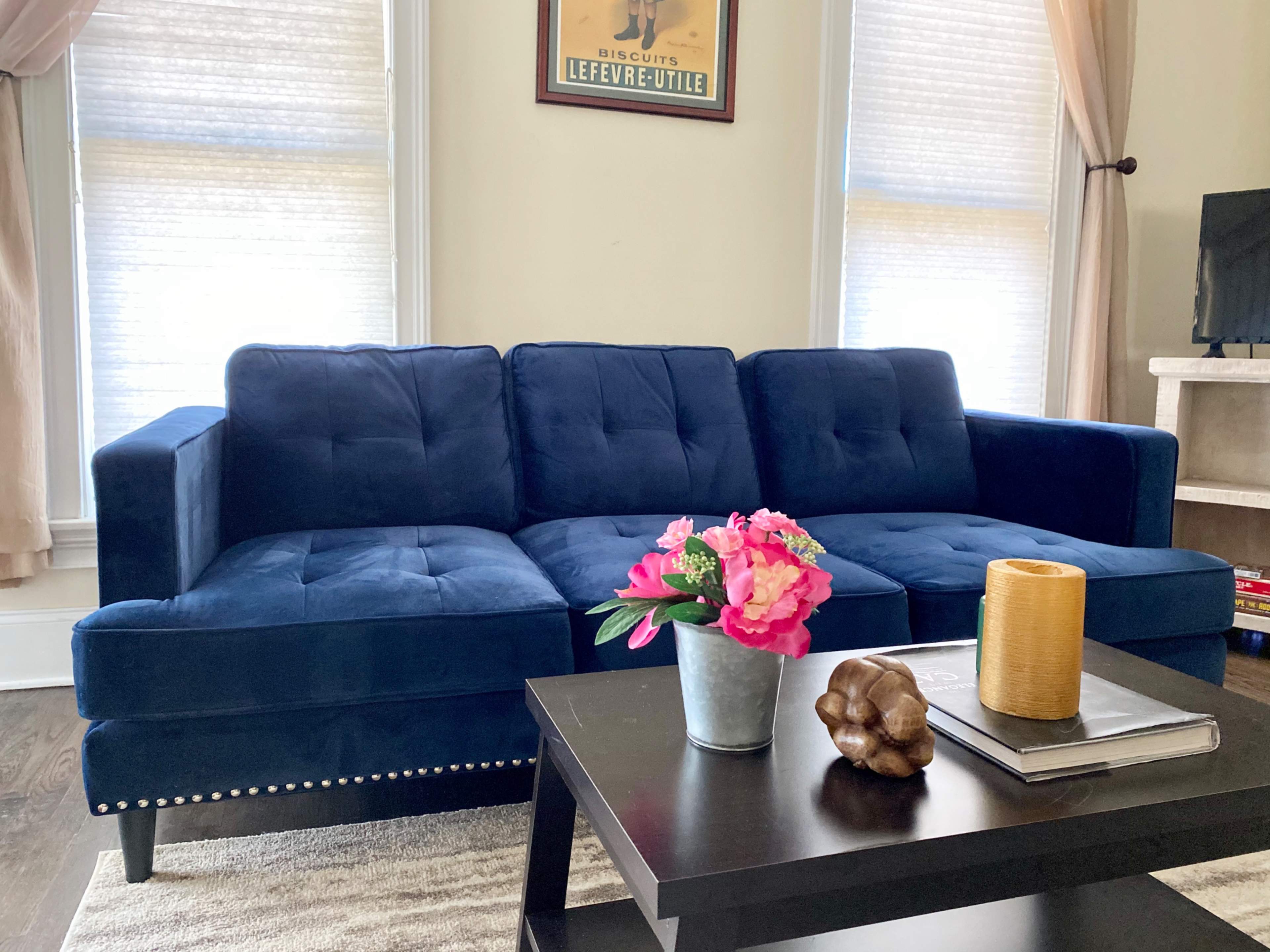 A navy blue sectional sofa with tufted upholstery is positioned near a coffee table adorned with a vase of pink flowers, a decorative wooden object, and a cylindrical candle holder.