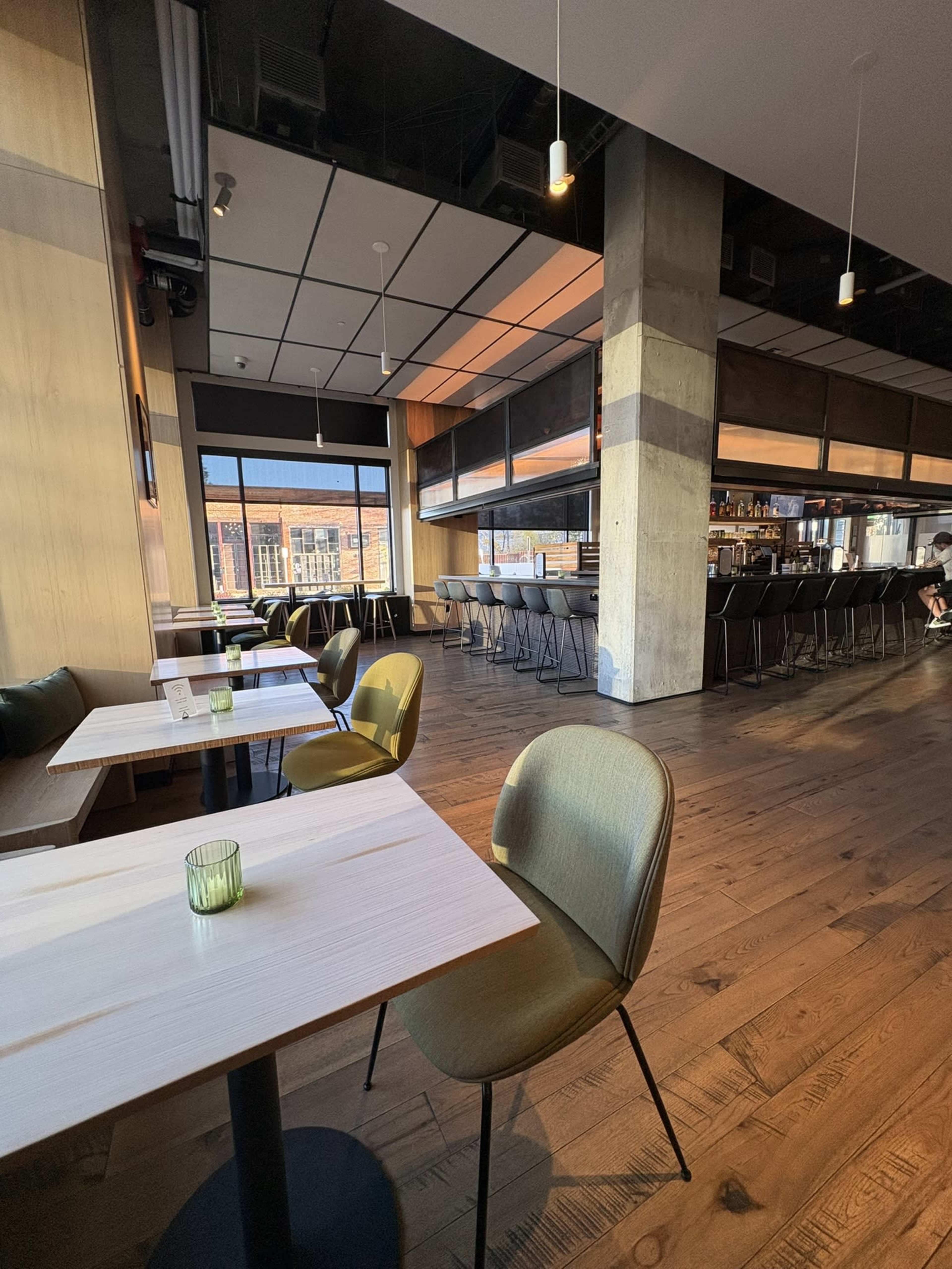 The image shows a modern restaurant interior with wooden floors, tables, and chairs, along with a bar area in the background.