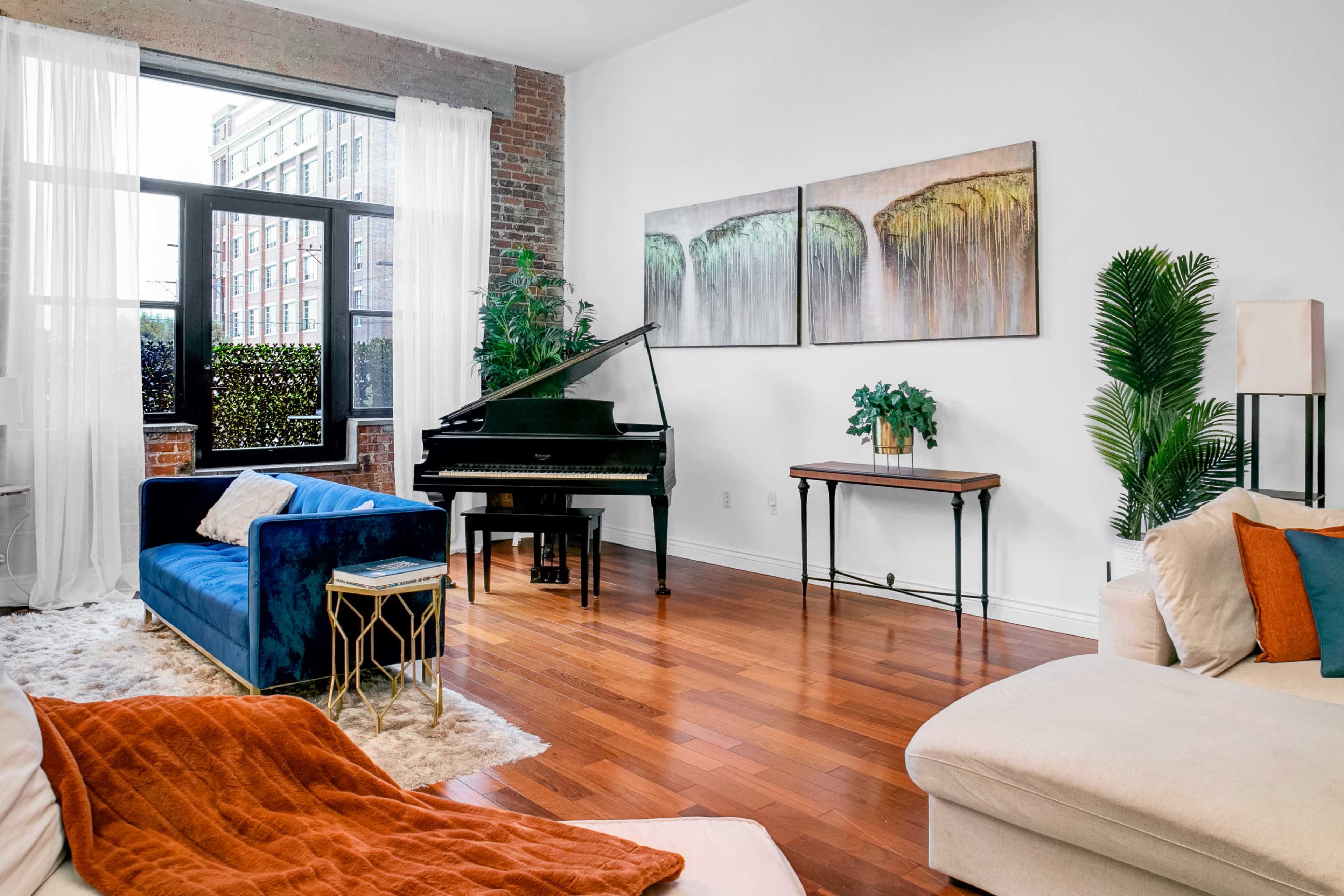 The scene features a modern living room with a grand piano, blue and beige sofas, and large windows allowing natural light to illuminate the space.