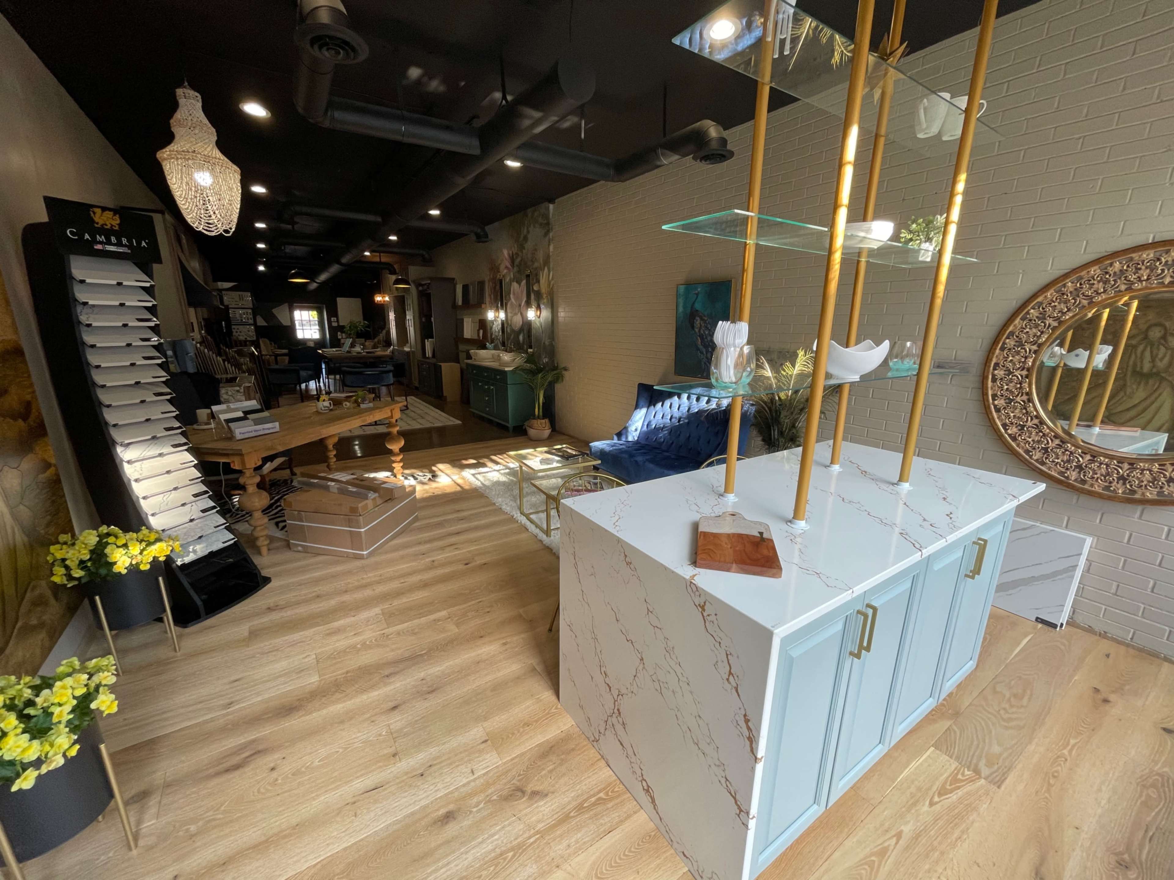 A modern retail space featuring a marble-topped display cabinet, wooden furniture, and decorative mirrors along the walls, with a combination of natural light and interior lighting.