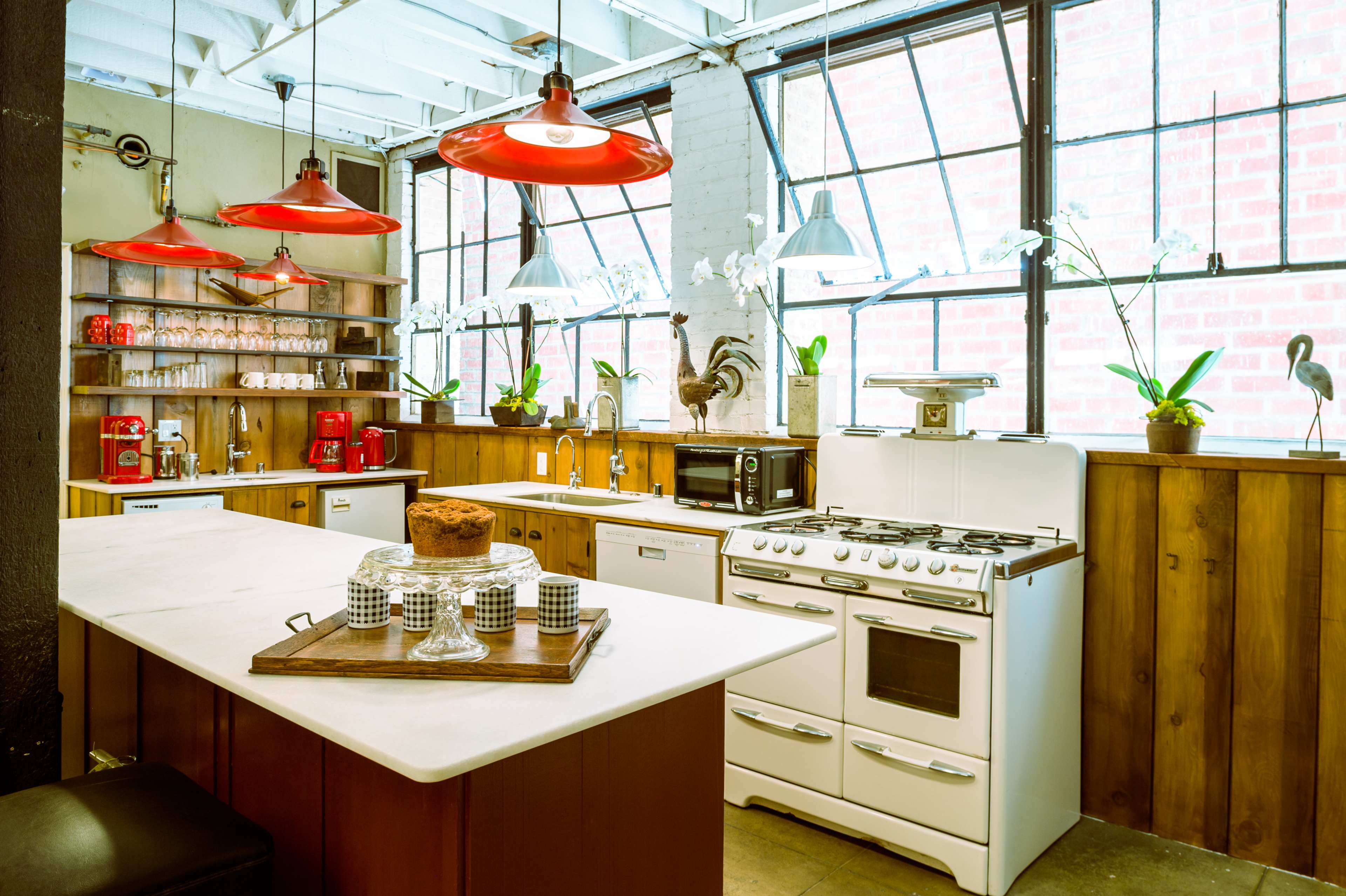 A modern kitchen with red pendant lights, wooden cabinetry, and a white stove, featuring large windows that let in natural light.