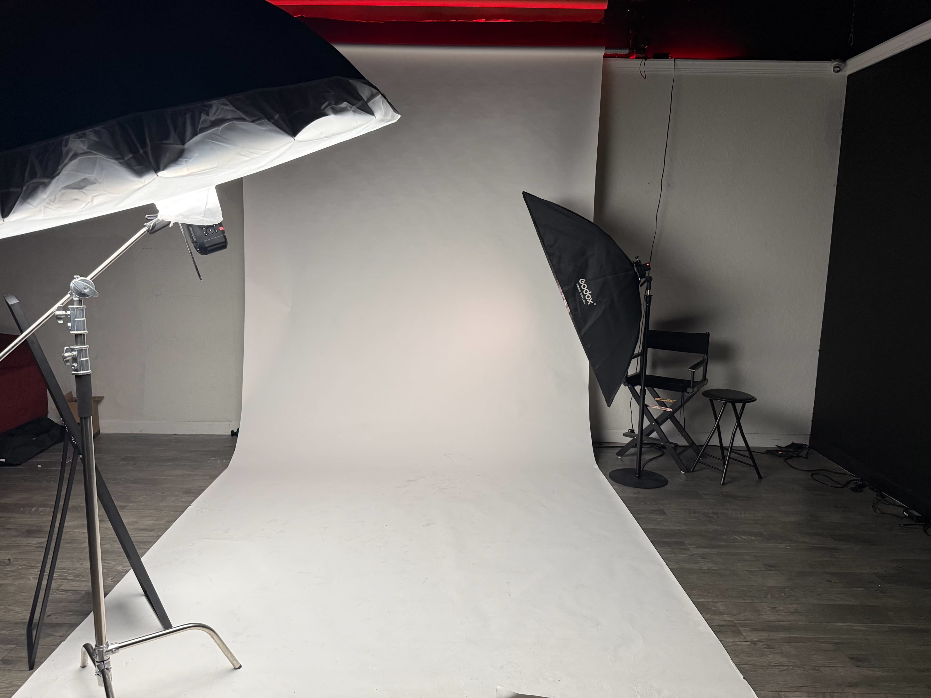 The image shows a photography studio with a white backdrop, softbox lighting, and a seating area.