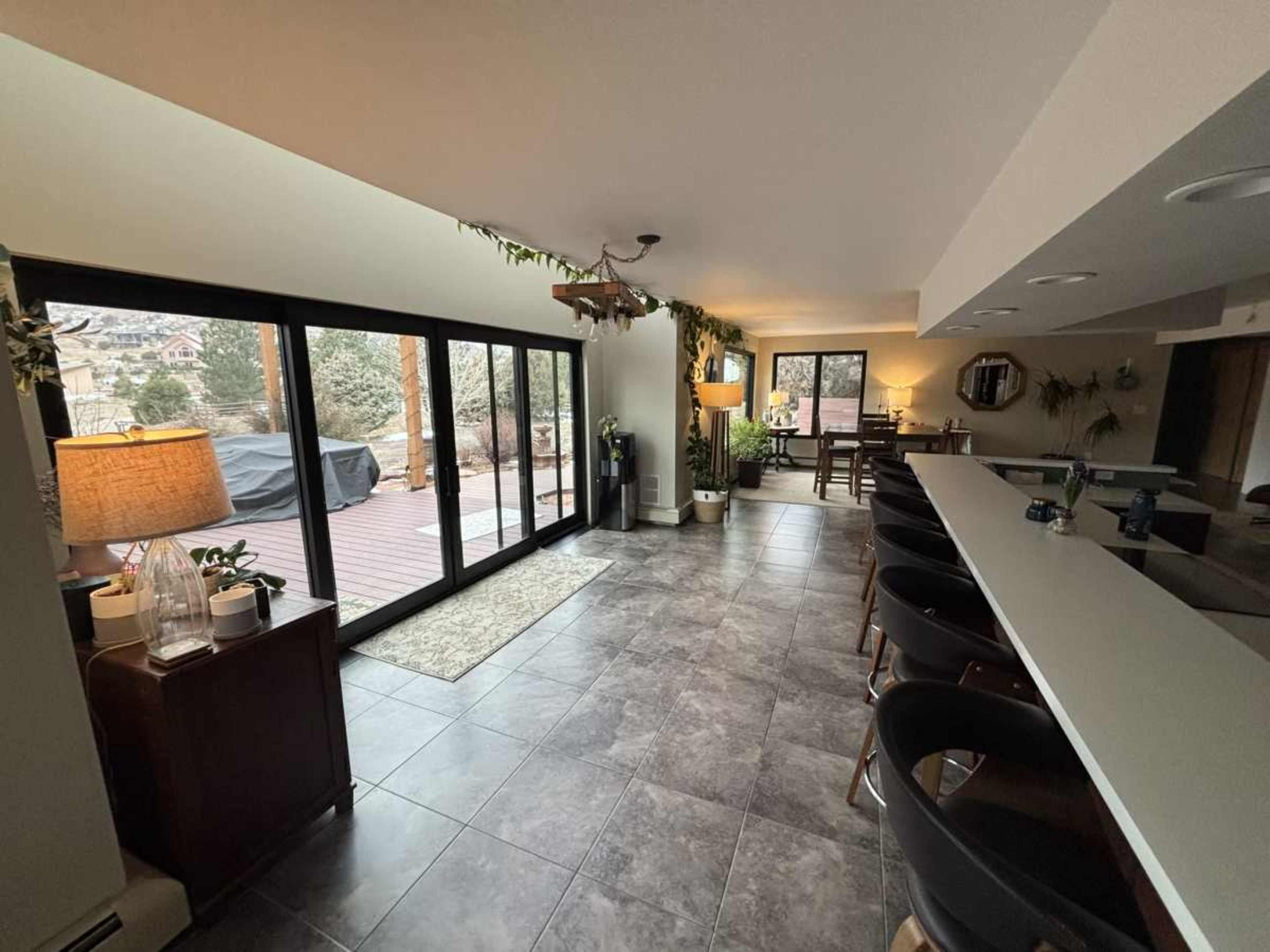 The image shows a spacious indoor area with large windows, a bar-style countertop, and a dining table visible in the background.