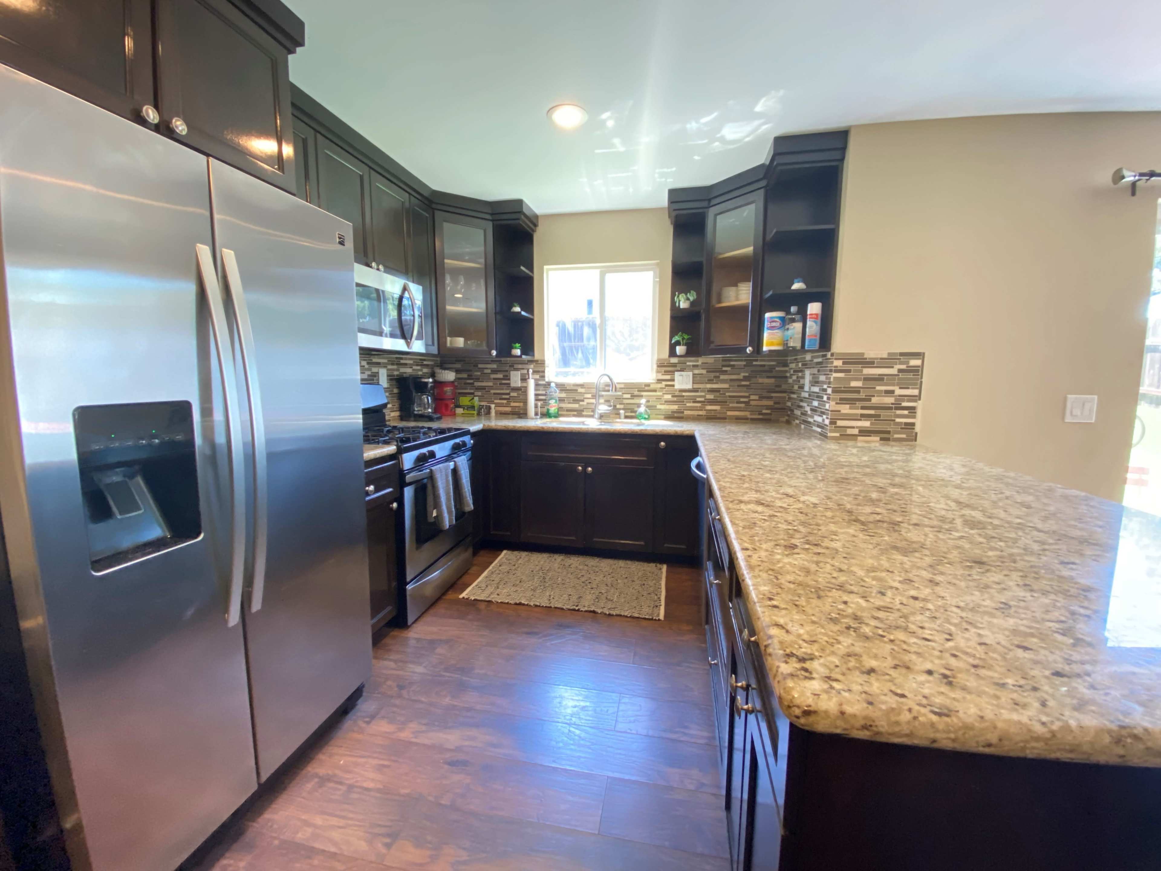 A modern kitchen featuring dark wooden cabinetry, stainless steel appliances, and a granite countertop.