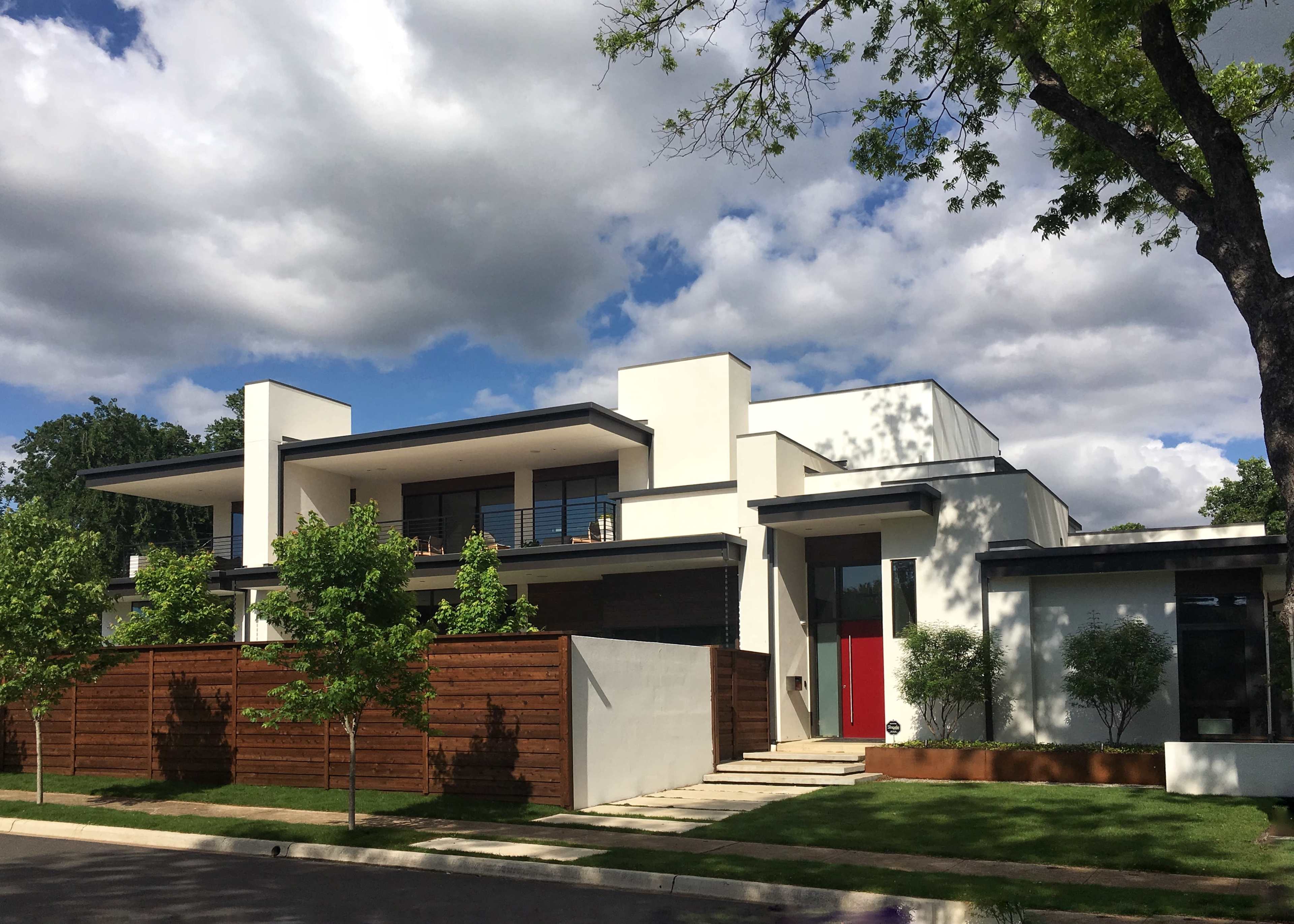 A modern two-story house features a red front door, large windows, and a wooden fence surrounding the yard.