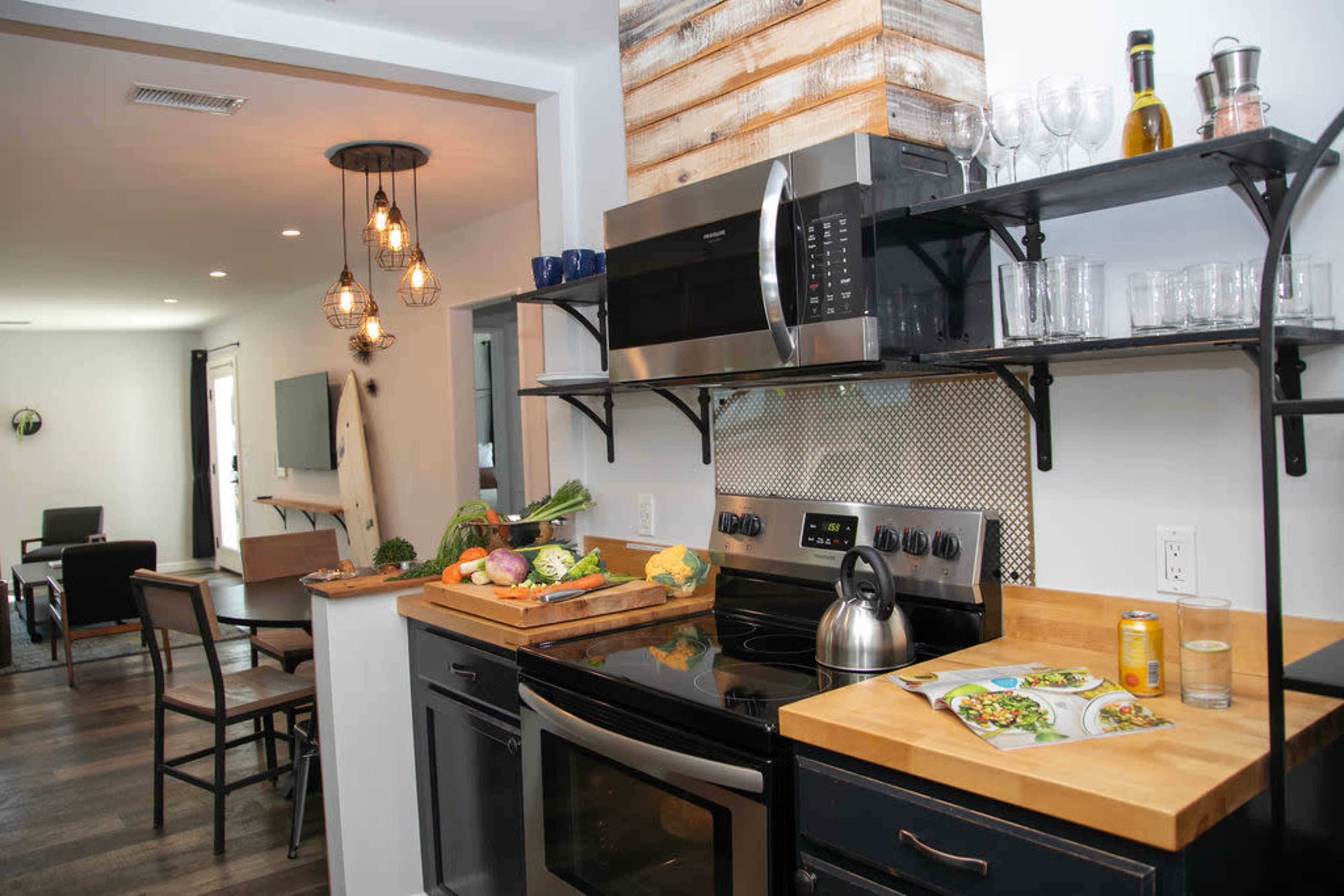 A modern kitchen features stainless steel appliances, a wooden countertop with fresh vegetables, and a dining area visible in the background.