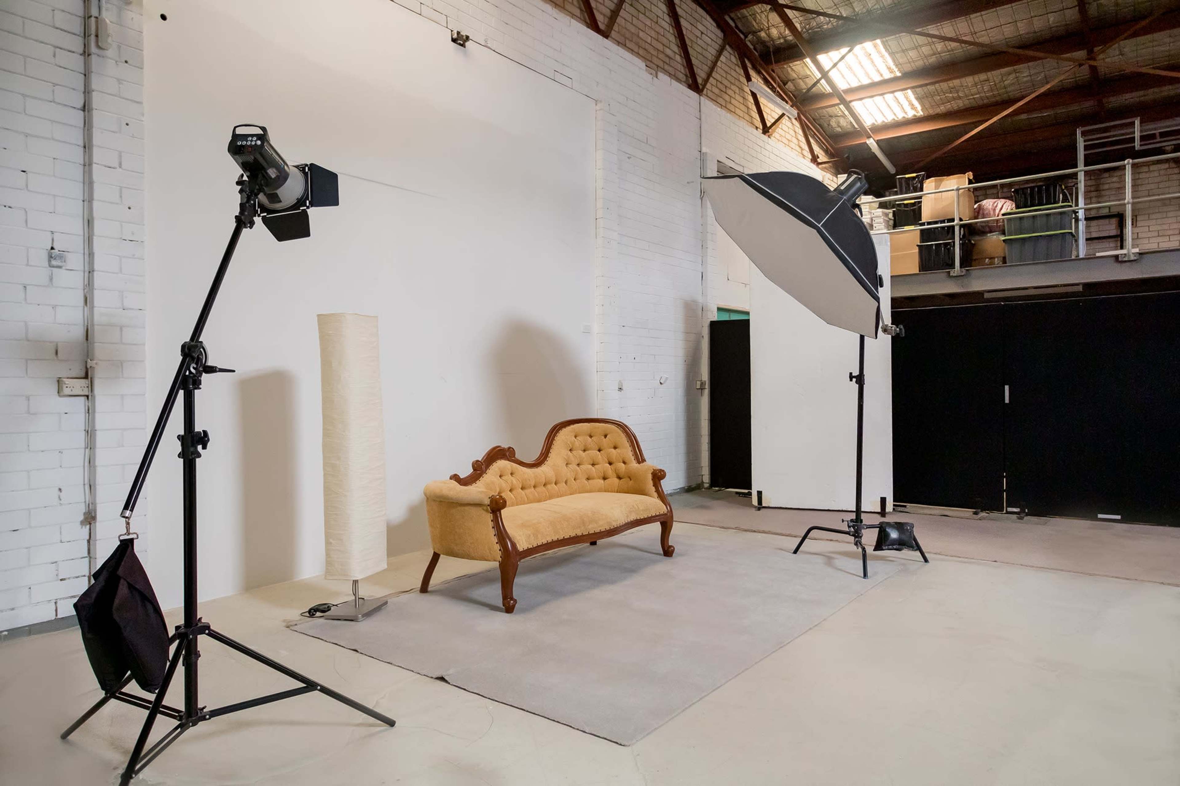 A photography studio setup featuring a vintage sofa on a rug, with two lighting fixtures and a plain backdrop.