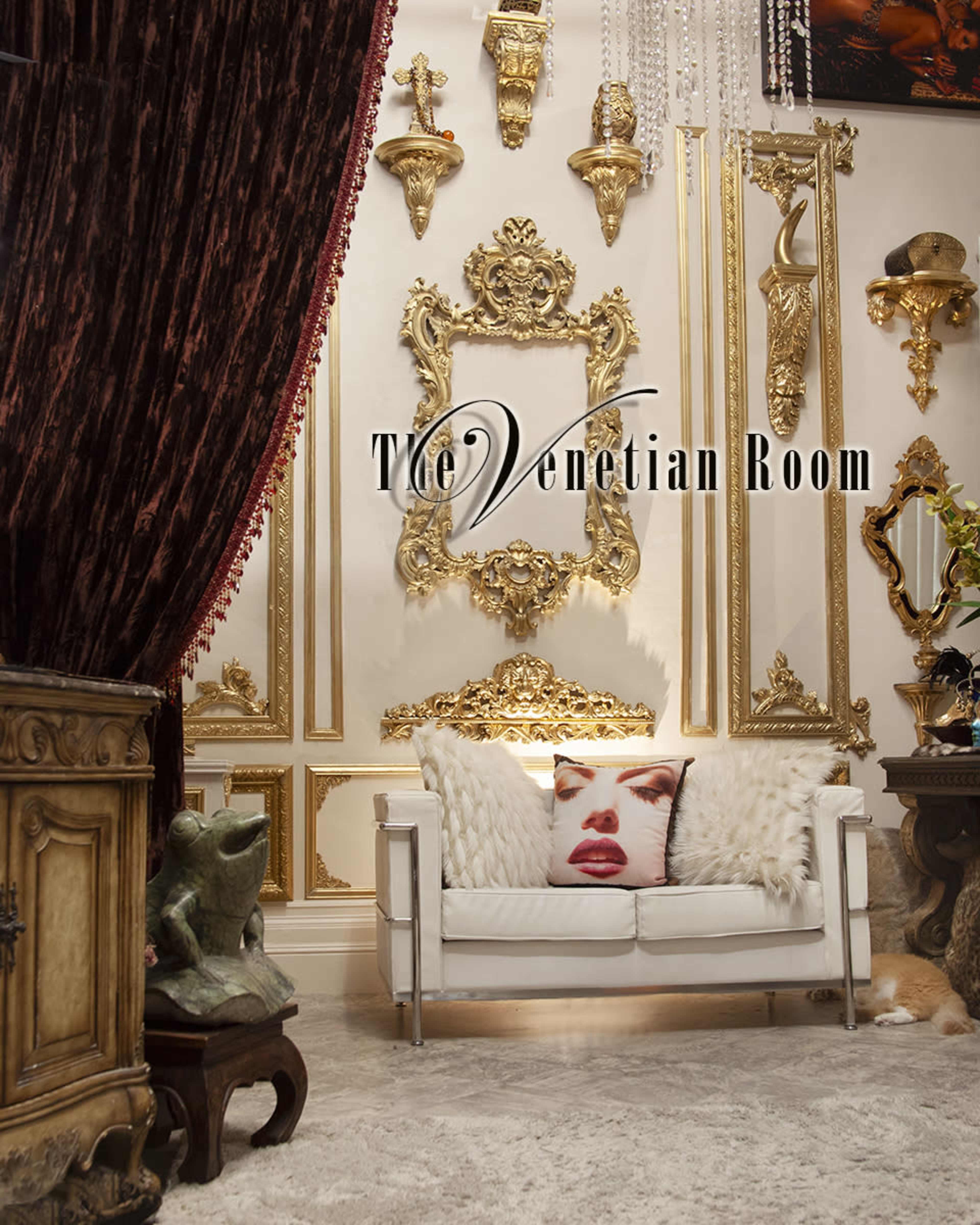 A lavishly decorated room features ornate gold wall decor, a plush white sofa, and rich burgundy drapes.