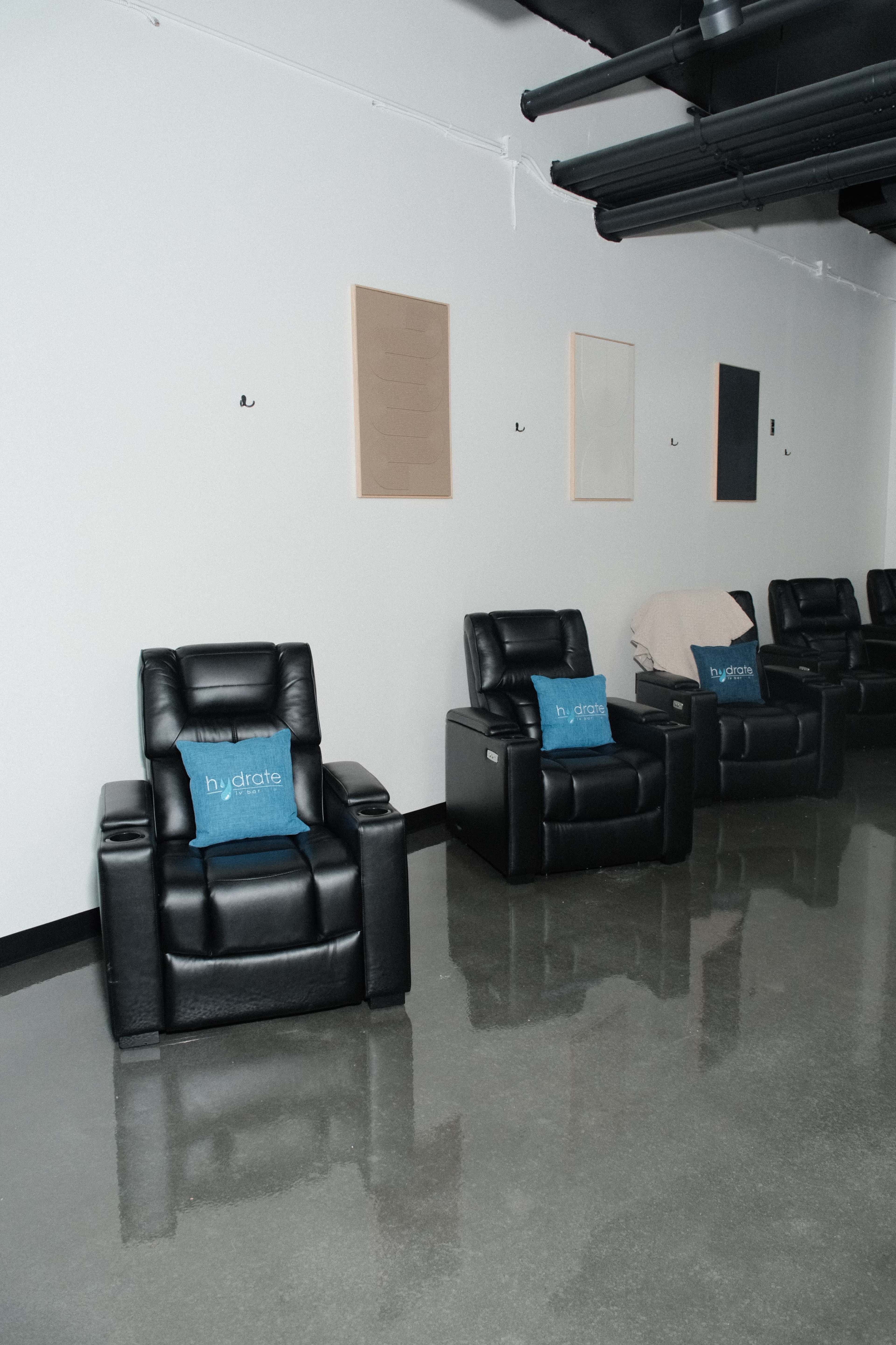 The image shows a row of black recliner chairs against a gray wall with a few simple, unframed artworks above them.