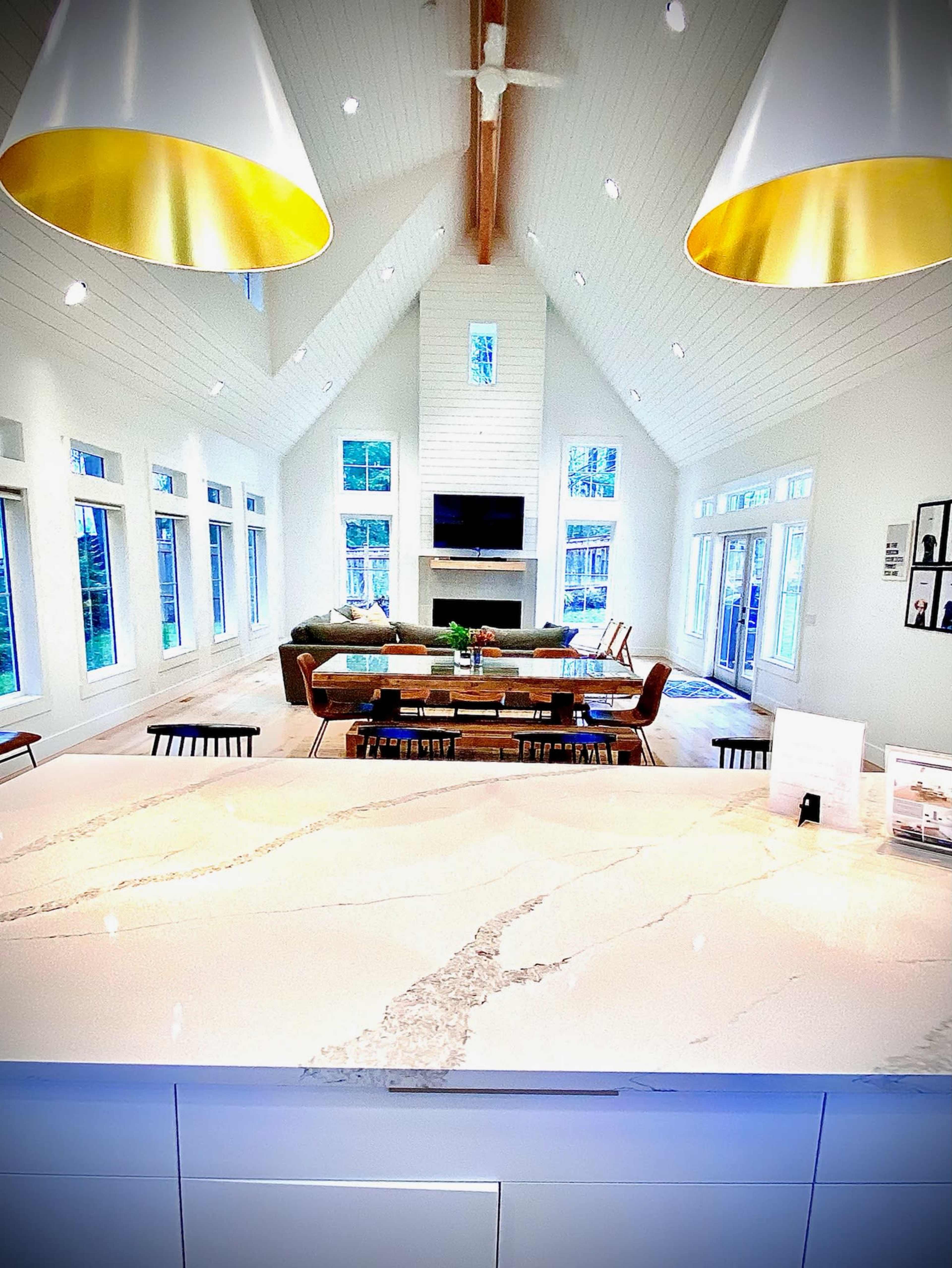 A spacious living area features tall ceilings, large windows, a dining table, and a modern kitchen with a marble countertop.