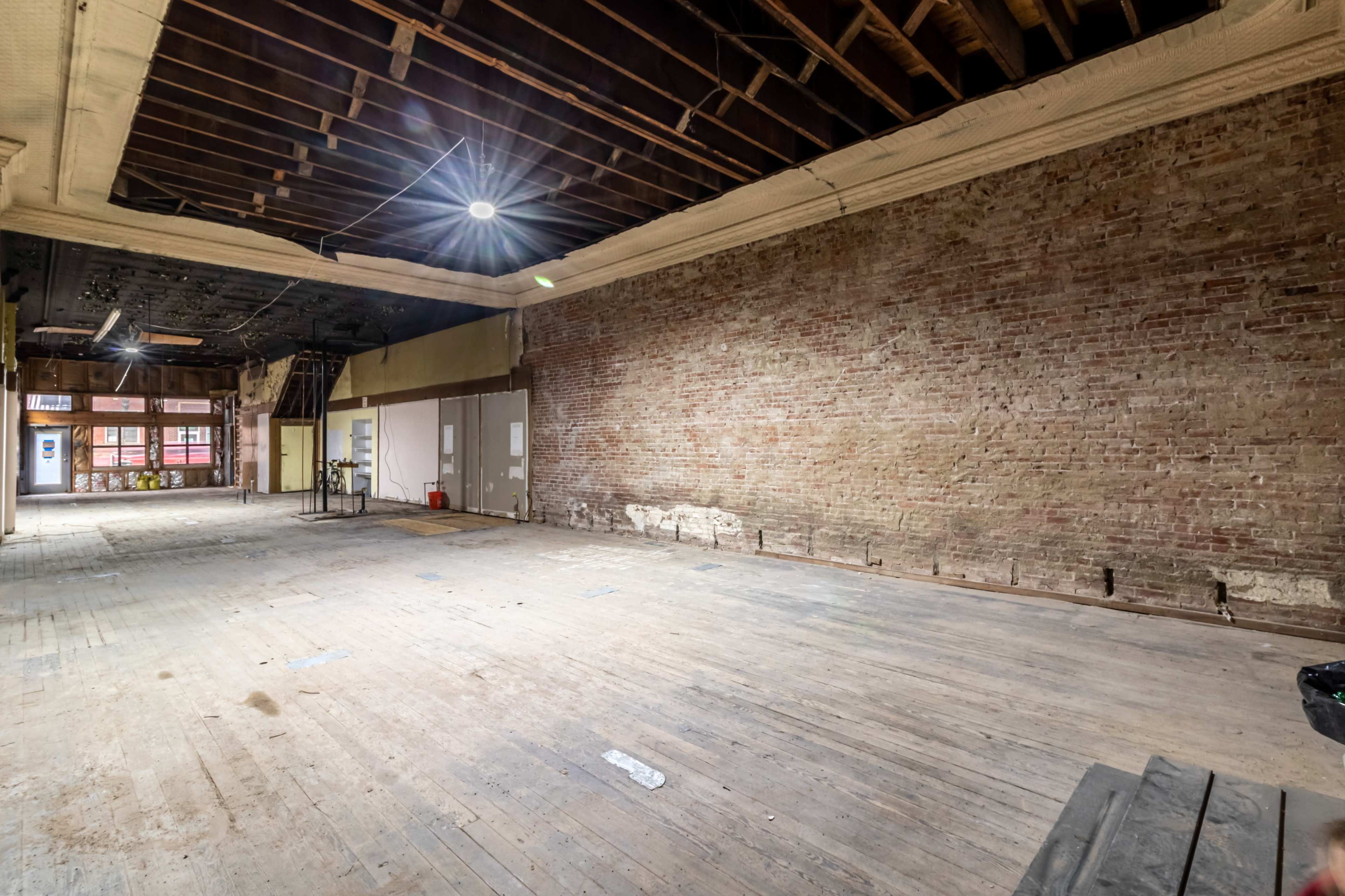 A spacious, empty room with exposed brick walls and wooden flooring under a ceiling with visible beams.