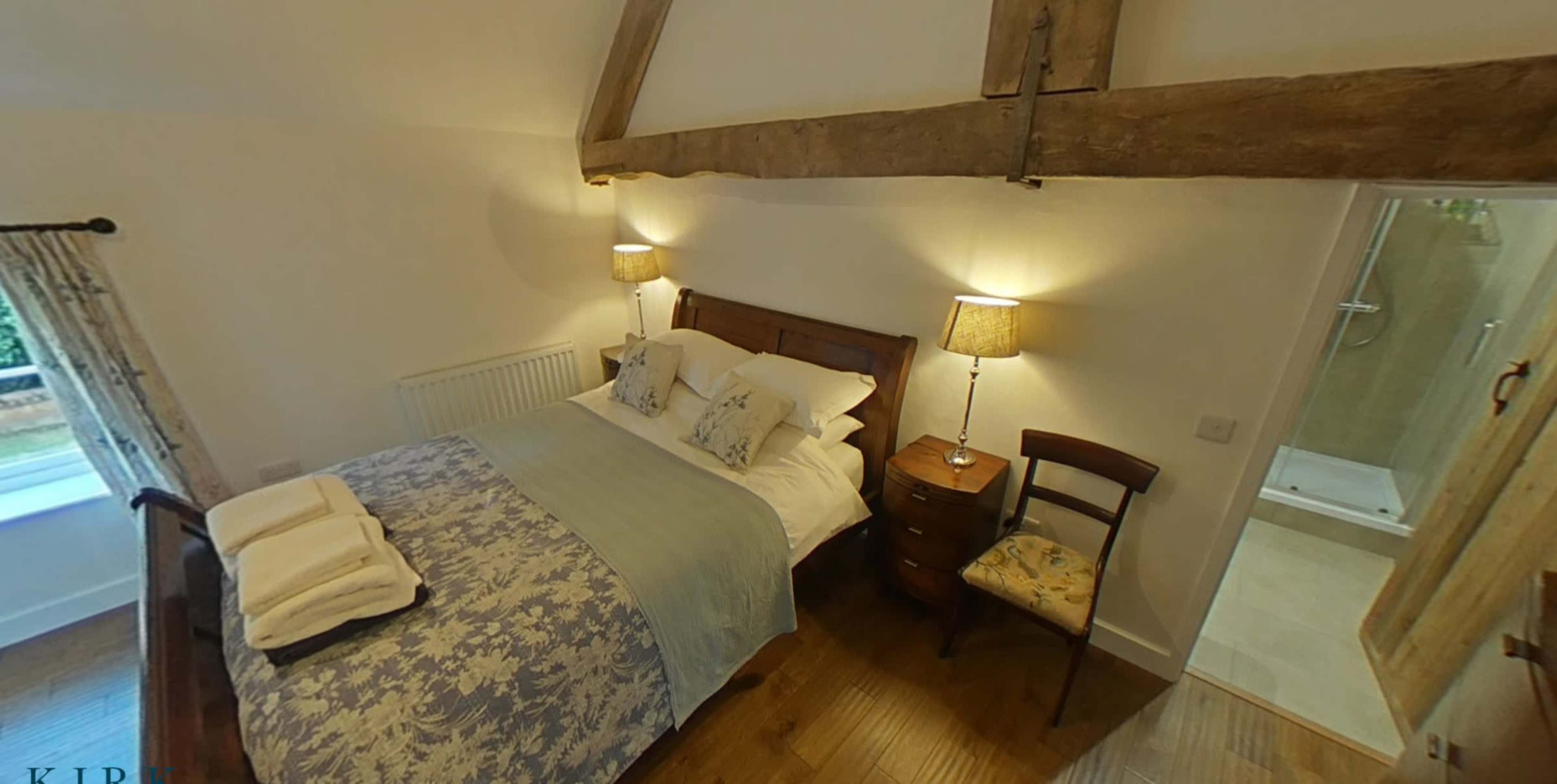 A cozy bedroom featuring a wooden bed, bedside lamps, a chair, and an en-suite bathroom.