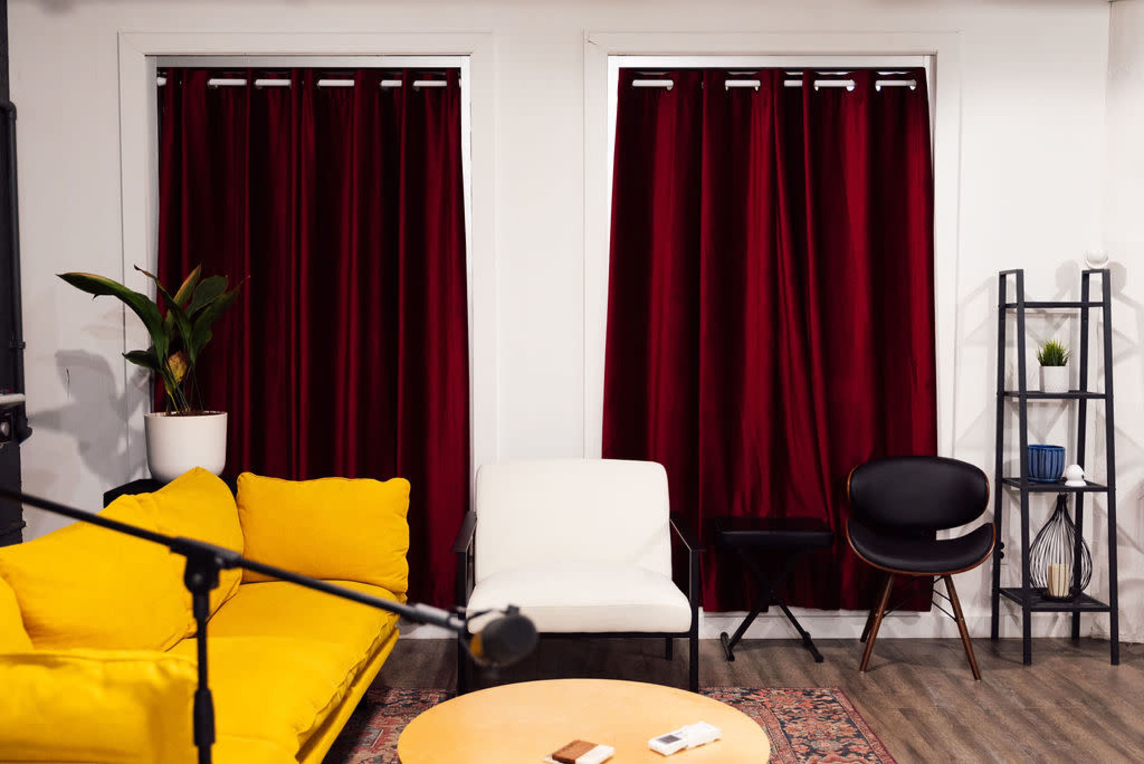A living room with a yellow sofa, a white chair, a round wooden coffee table, and two large red curtains covering windows.