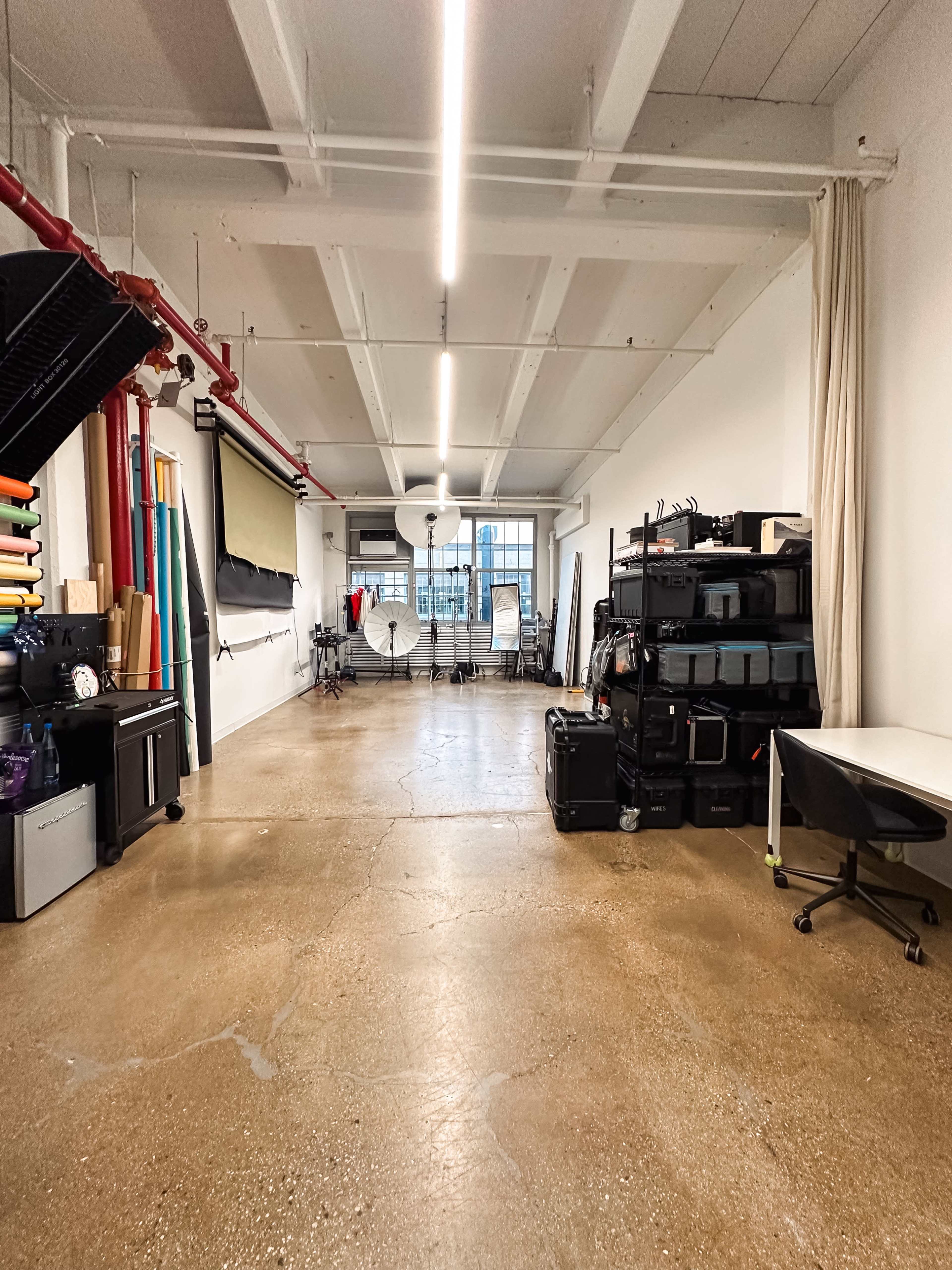 A spacious studio with concrete floors, a variety of equipment, and large windows providing natural light.