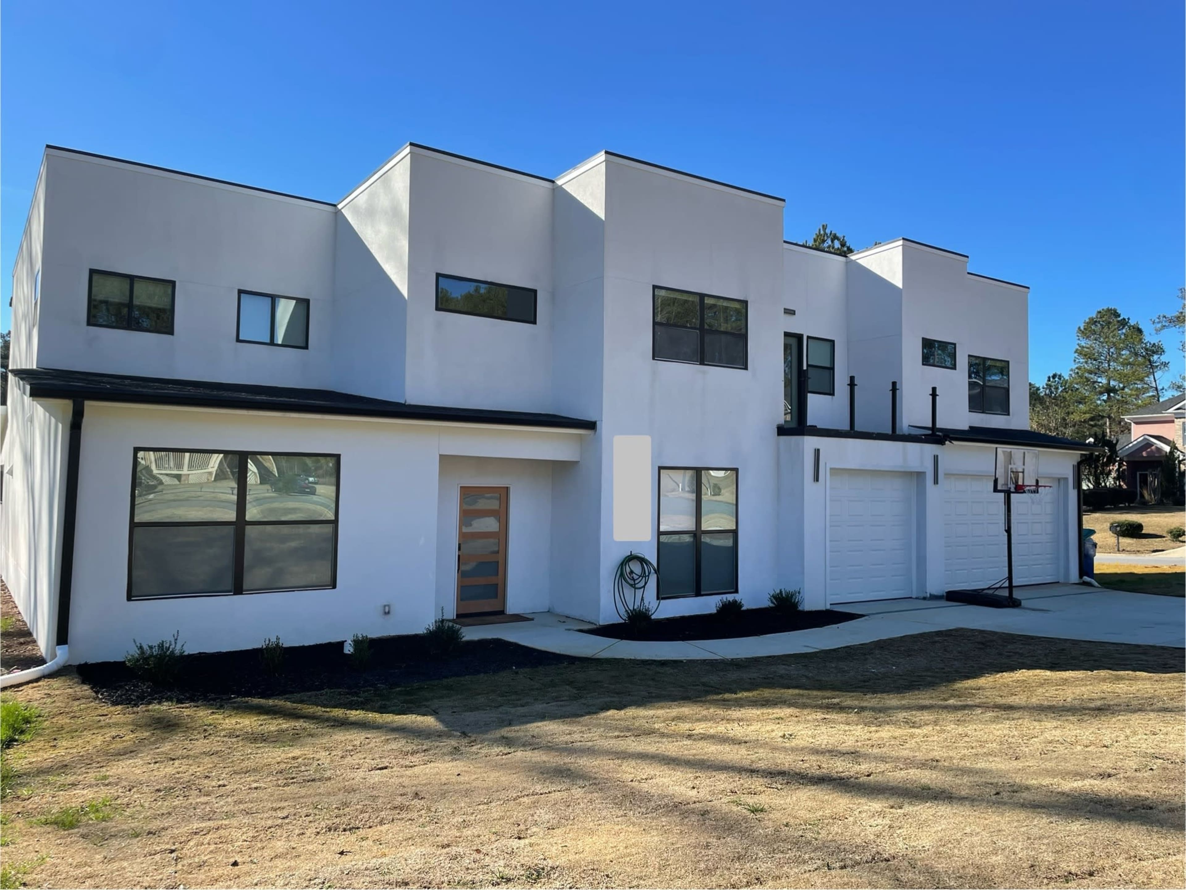The image shows a modern, two-story house with a white exterior, large windows, and a driveway featuring a basketball hoop.