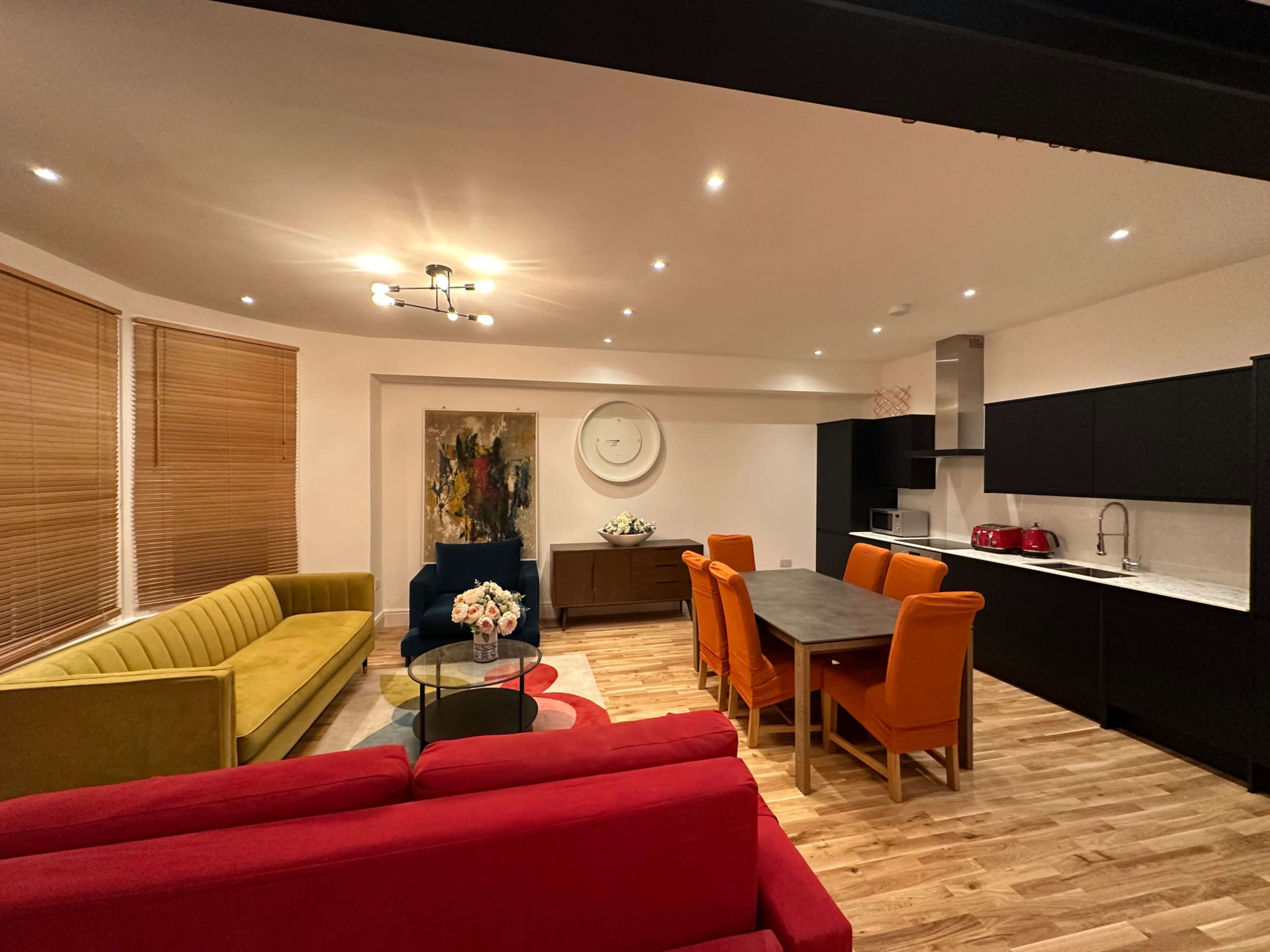 A modern living space featuring colorful seating arrangements, a dining table, and a well-equipped kitchen.