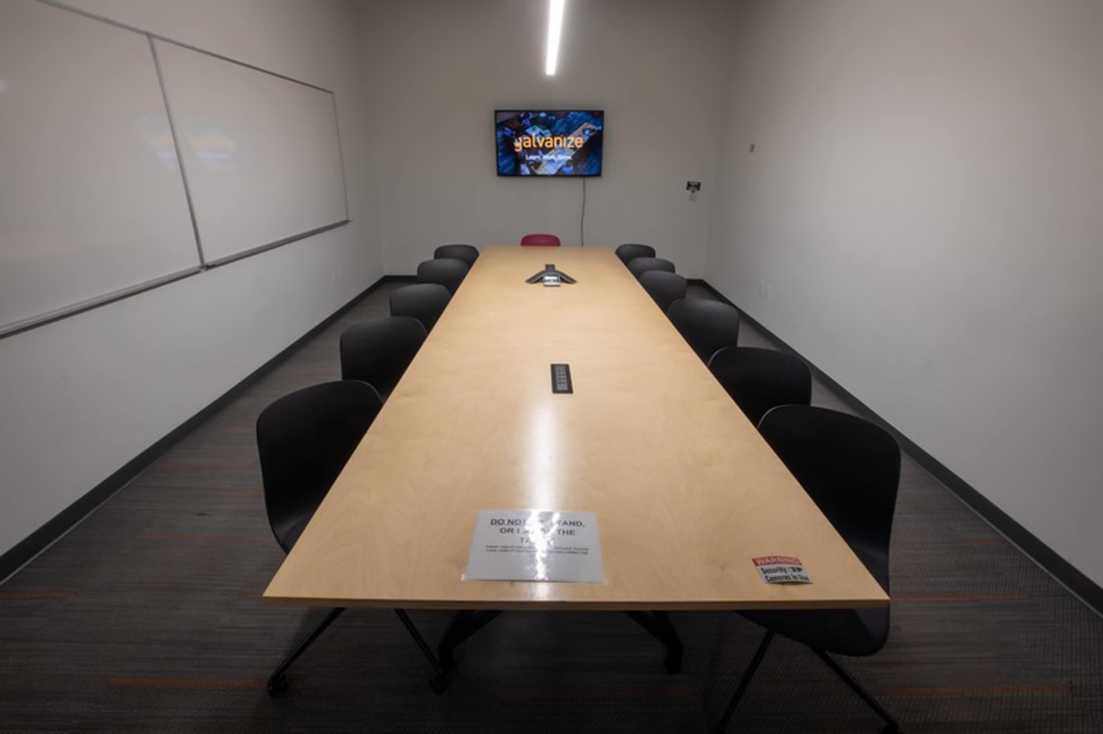 A long conference table with black chairs surrounds it, set in a meeting room featuring a screen displaying the word "advance."