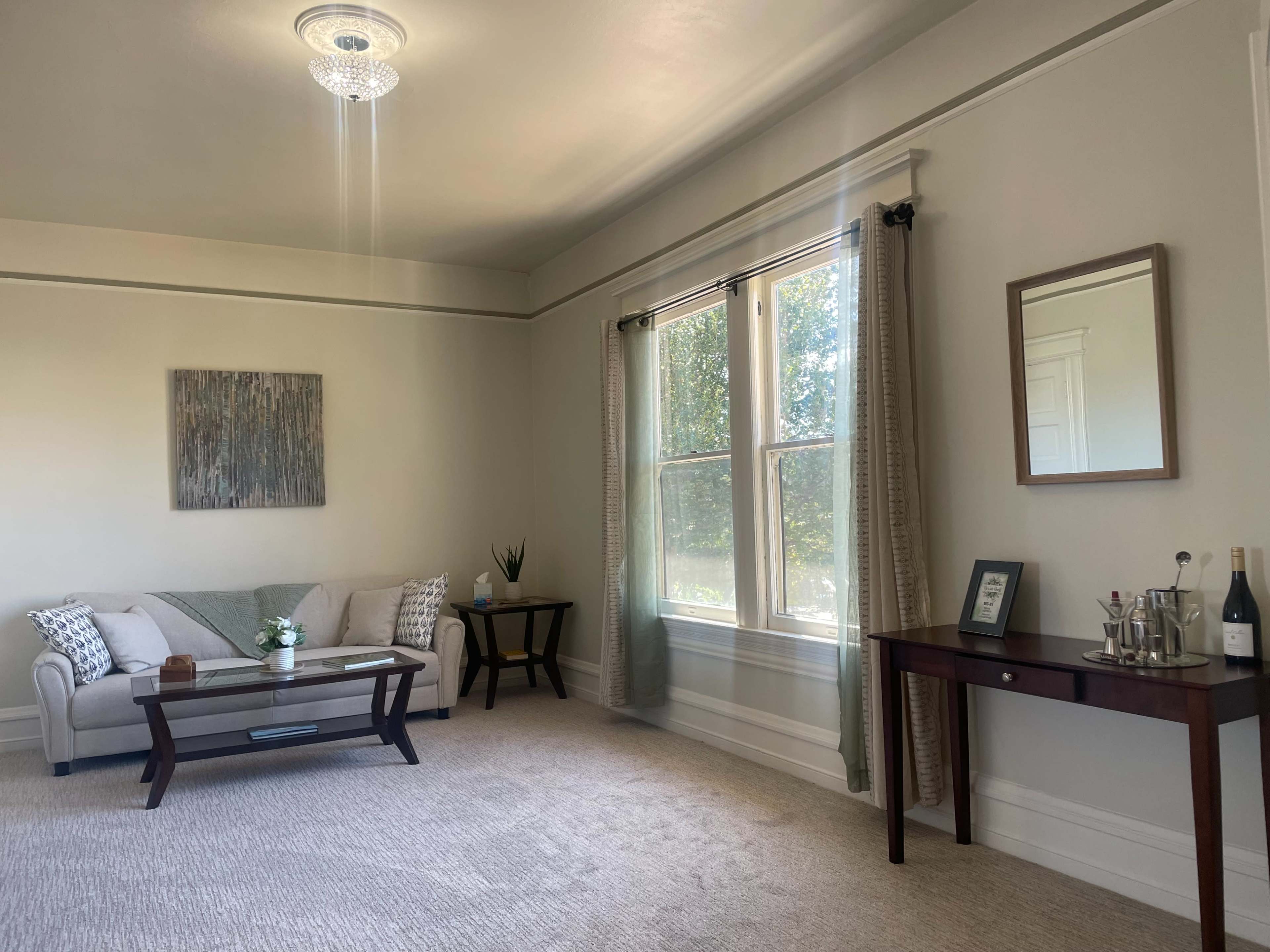 A well-lit living room with a sofa, coffee table, side table with a decorative arrangement, and large windows letting in natural light.