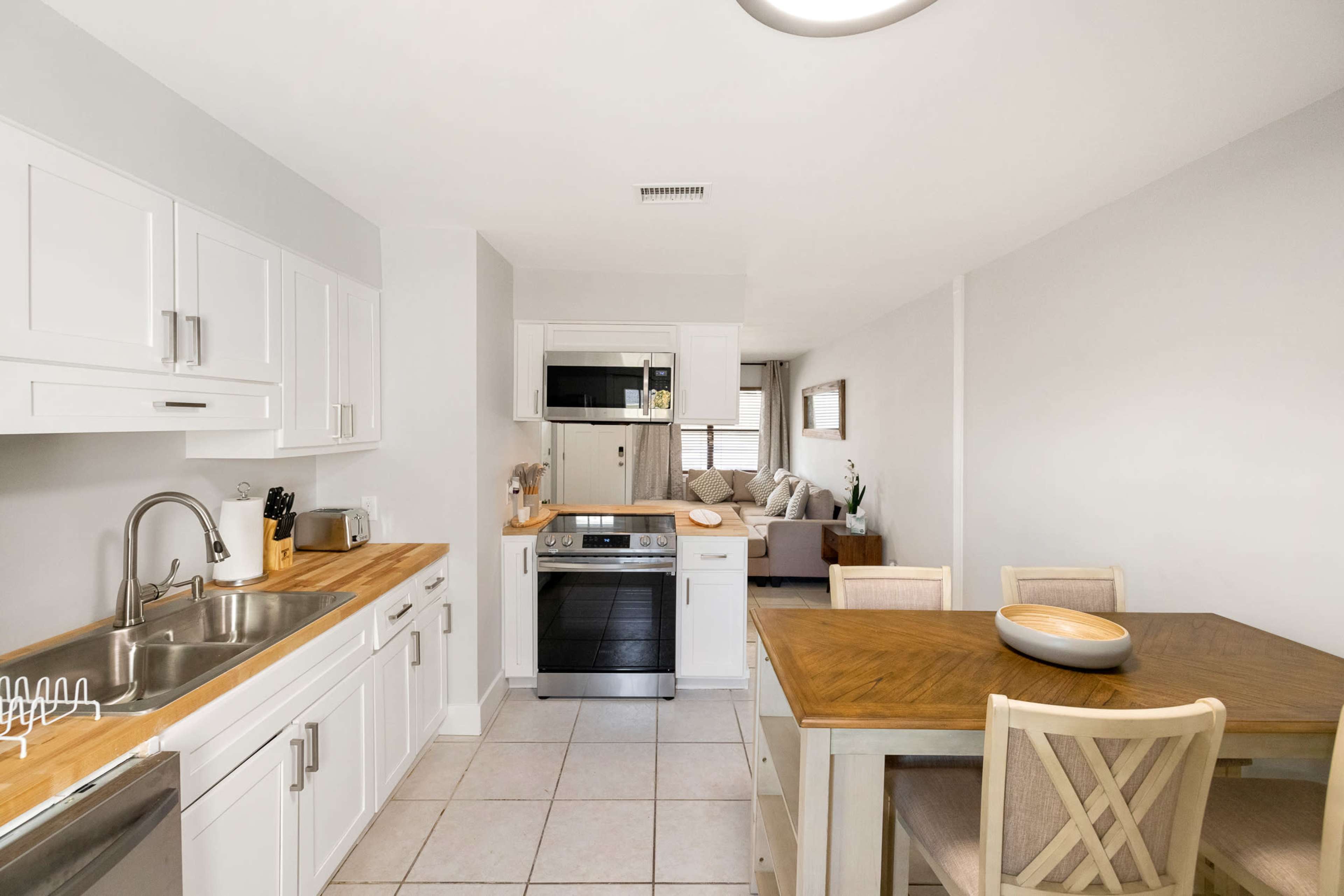A modern kitchen features white cabinetry, stainless steel appliances, and a wooden dining table with chairs.