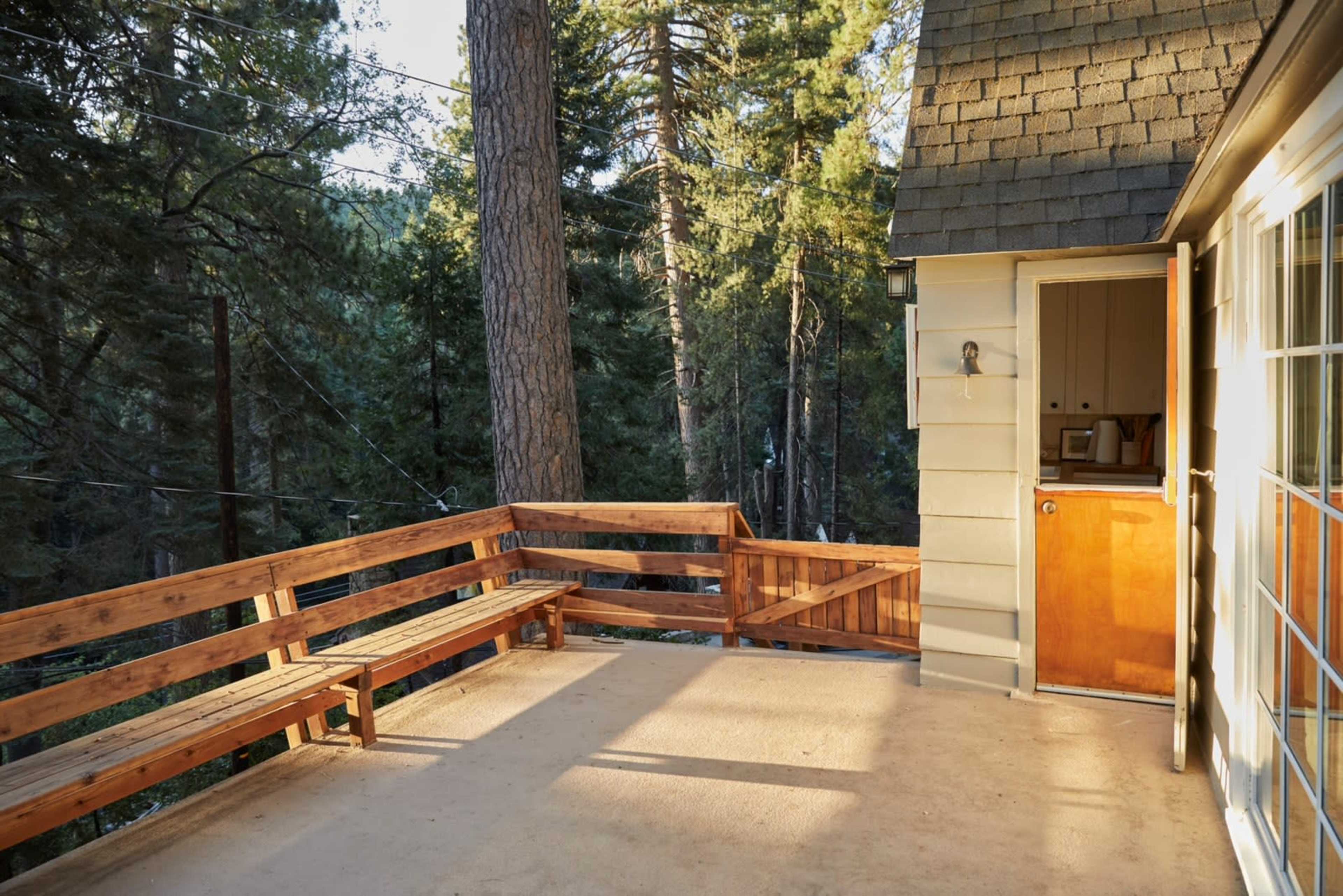A wooden deck extends from a cabin, surrounded by tall trees in a forested area.
