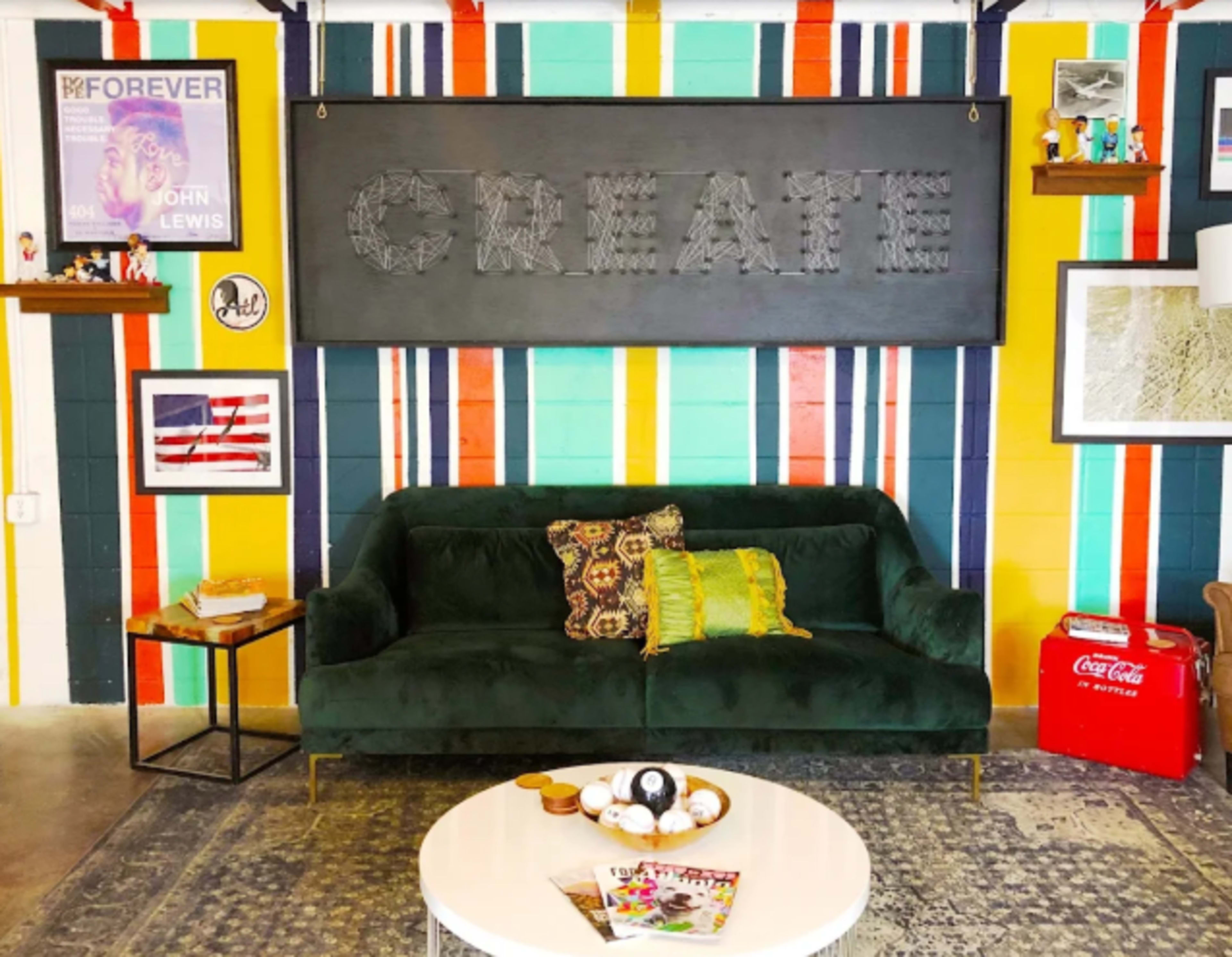 The image shows a vibrant room featuring a green couch, a large "CREATE" sign, and colorful striped walls with various decorations and items on display.