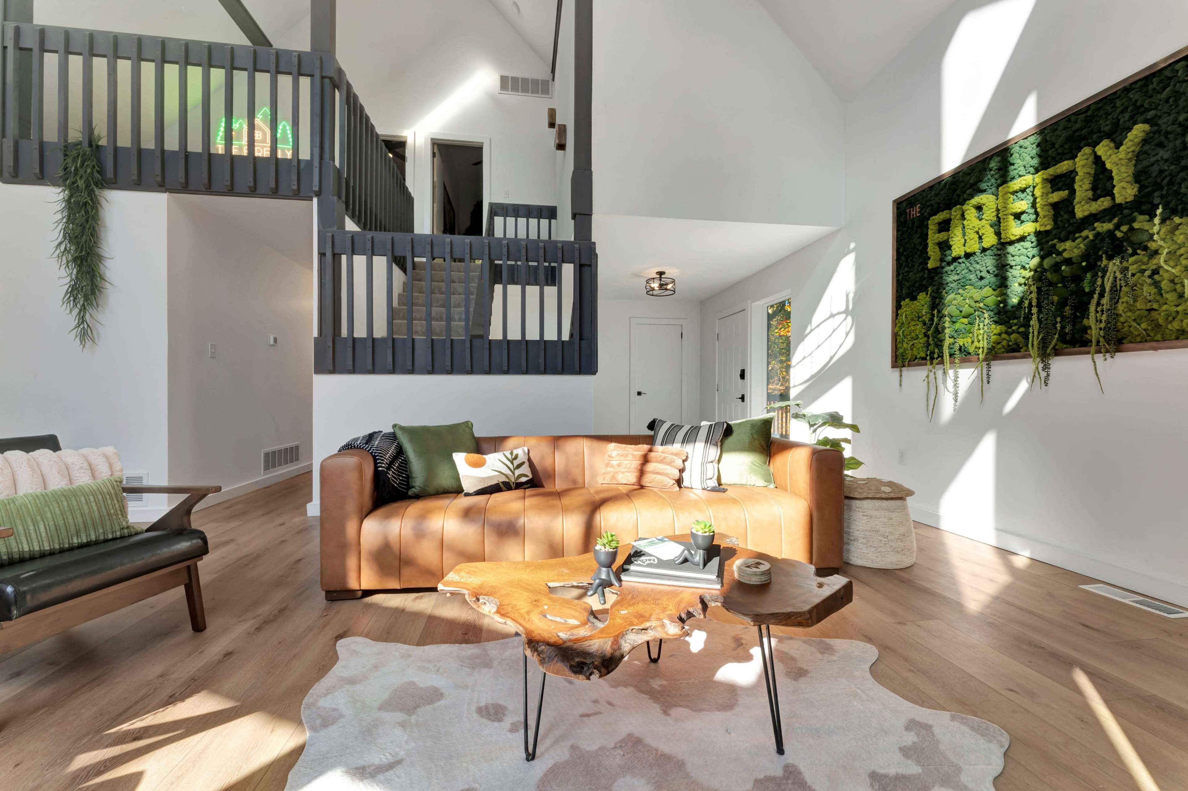 The image shows a modern living room featuring a brown leather sofa, a wooden coffee table, and a vibrant wall display of greenery.