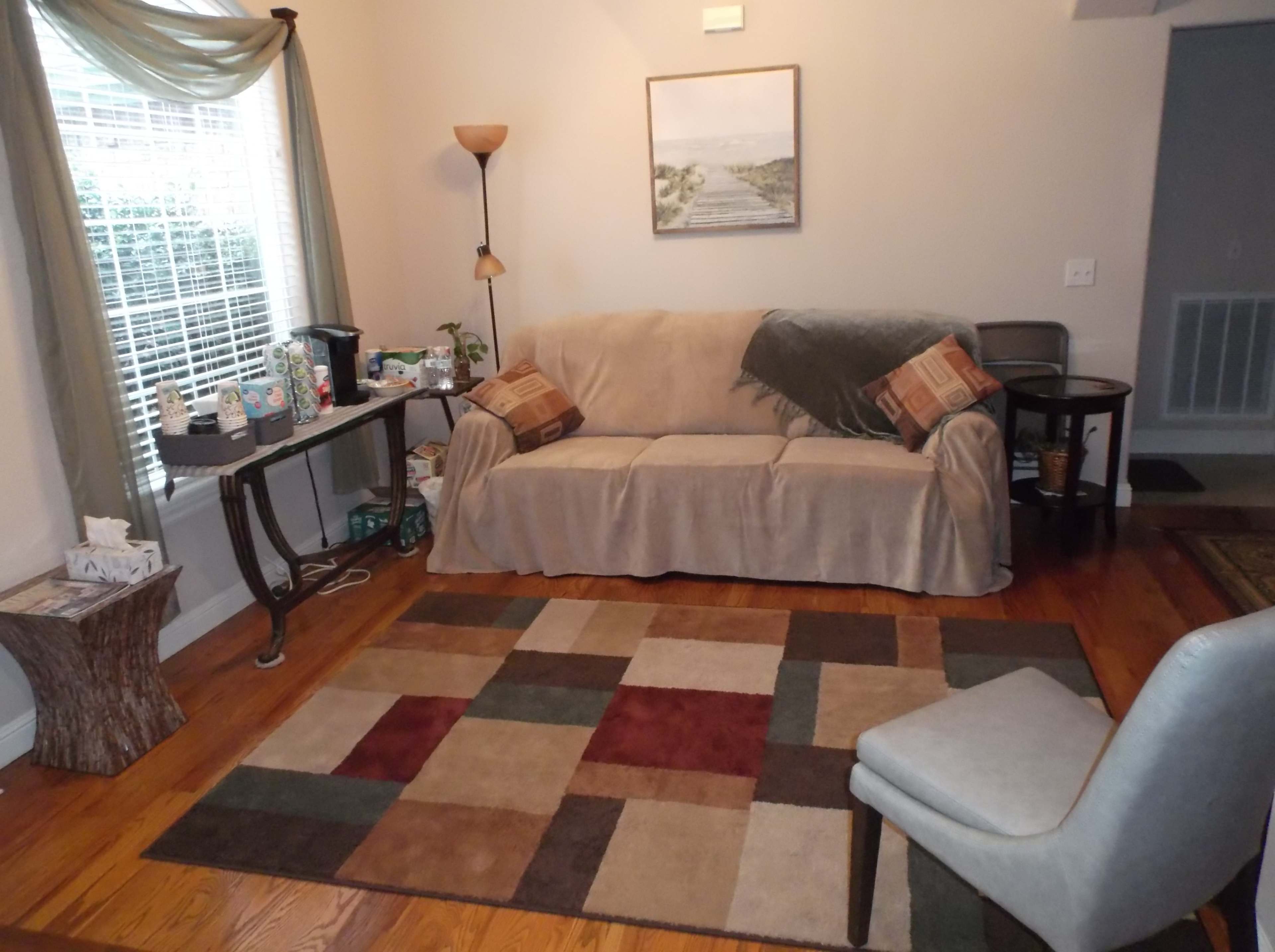 A cozy living room with a beige couch, a patterned rug, and a small table beside a window.