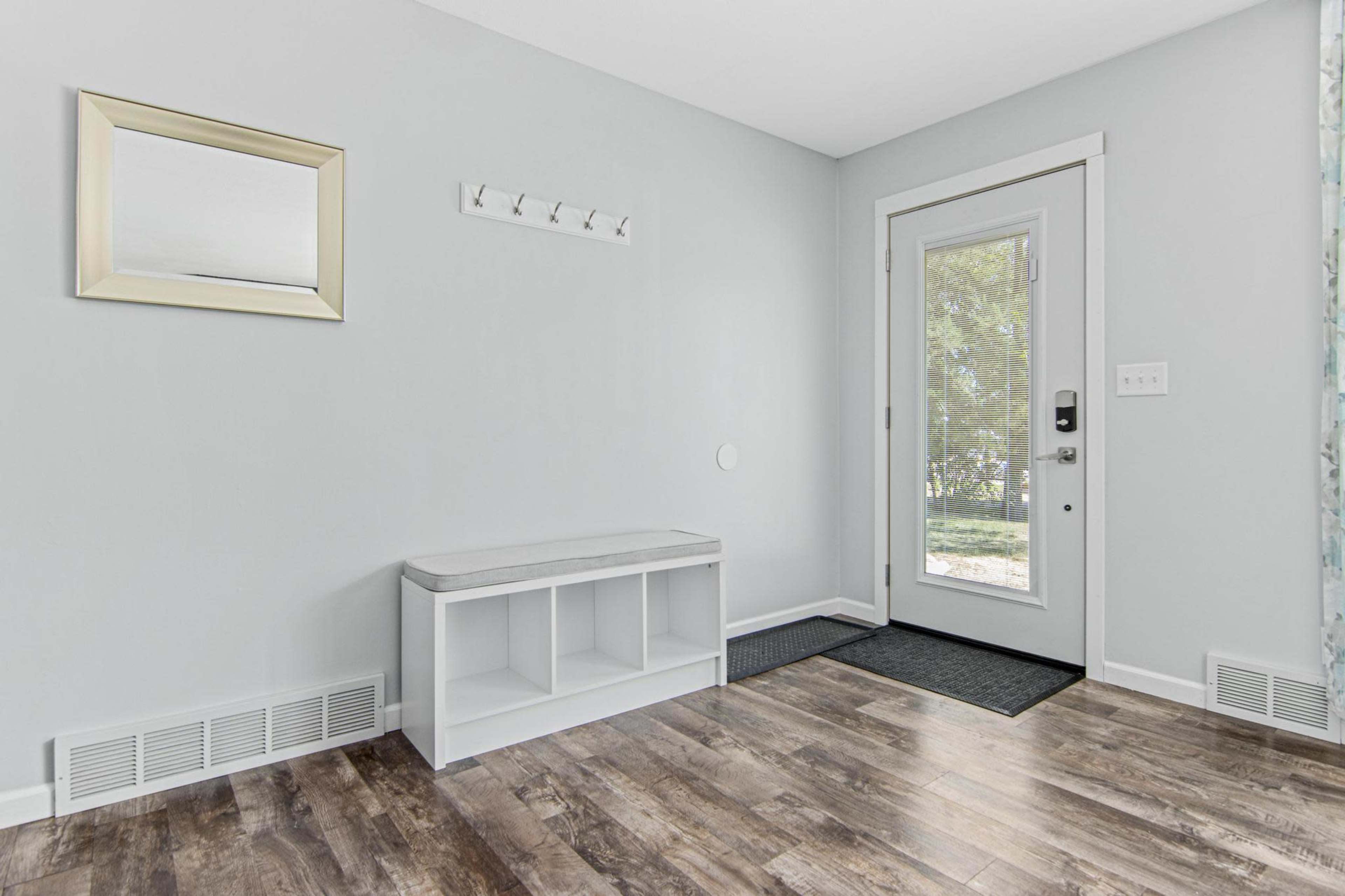 A minimalist entryway with a bench, coat hooks, a mirror, and a door leading outside.