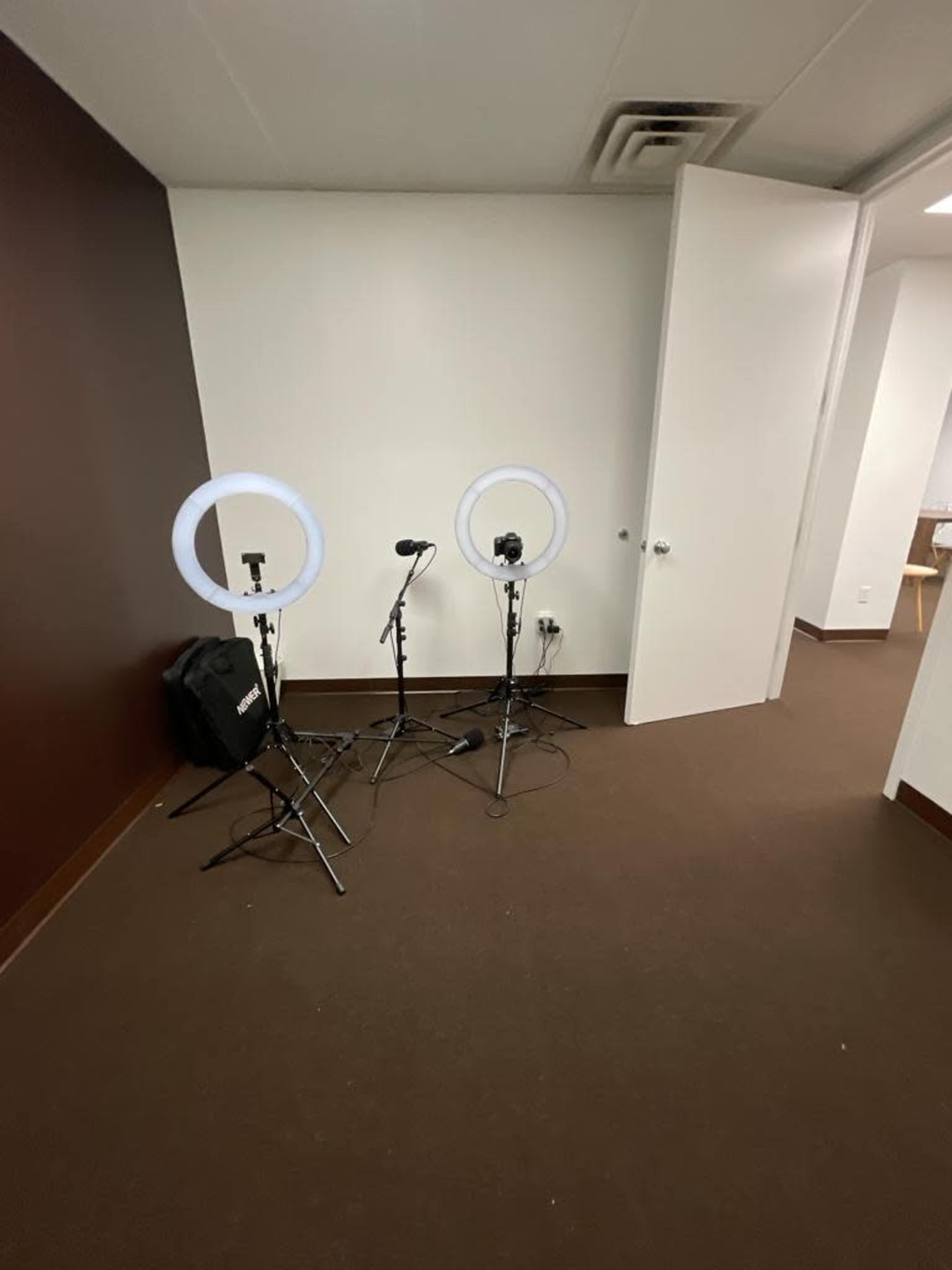 A small, empty room with two ring lights and microphones set on tripods.
