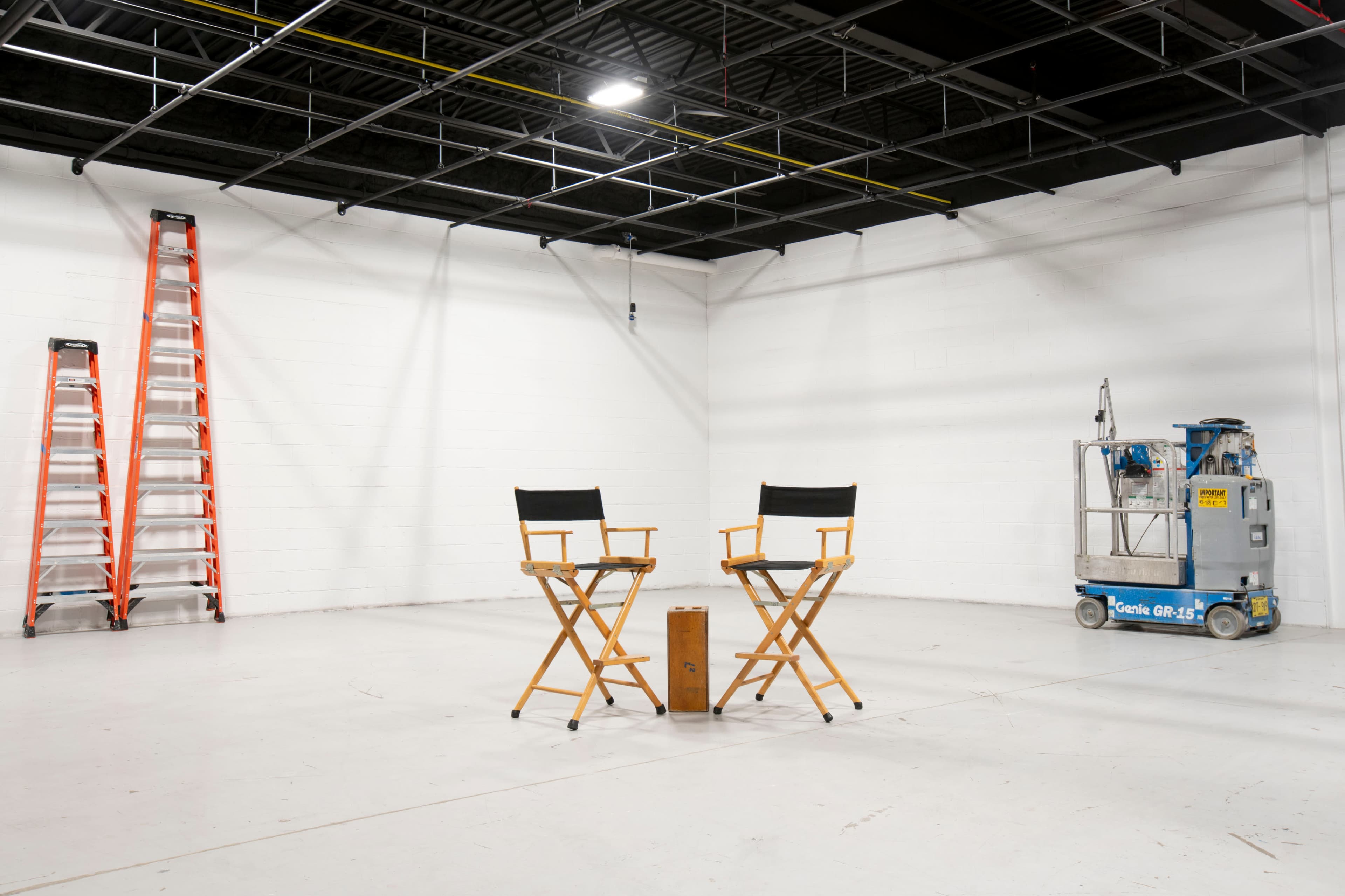 Two director's chairs placed on a bare concrete floor, accompanied by a small table and a ladder against the wall.