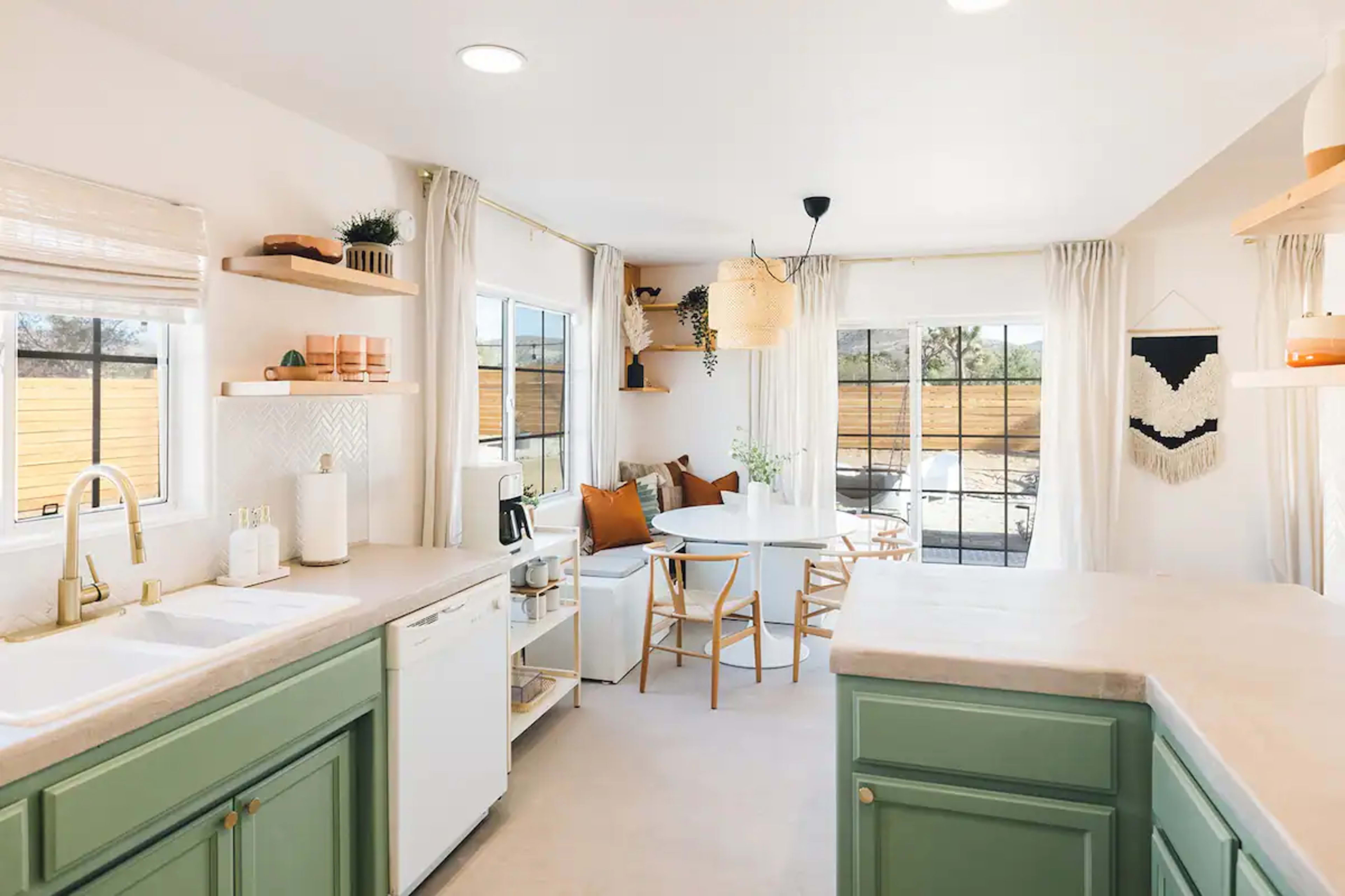 A modern kitchen features green cabinetry, a dining table with chairs, and ample natural light from large windows.