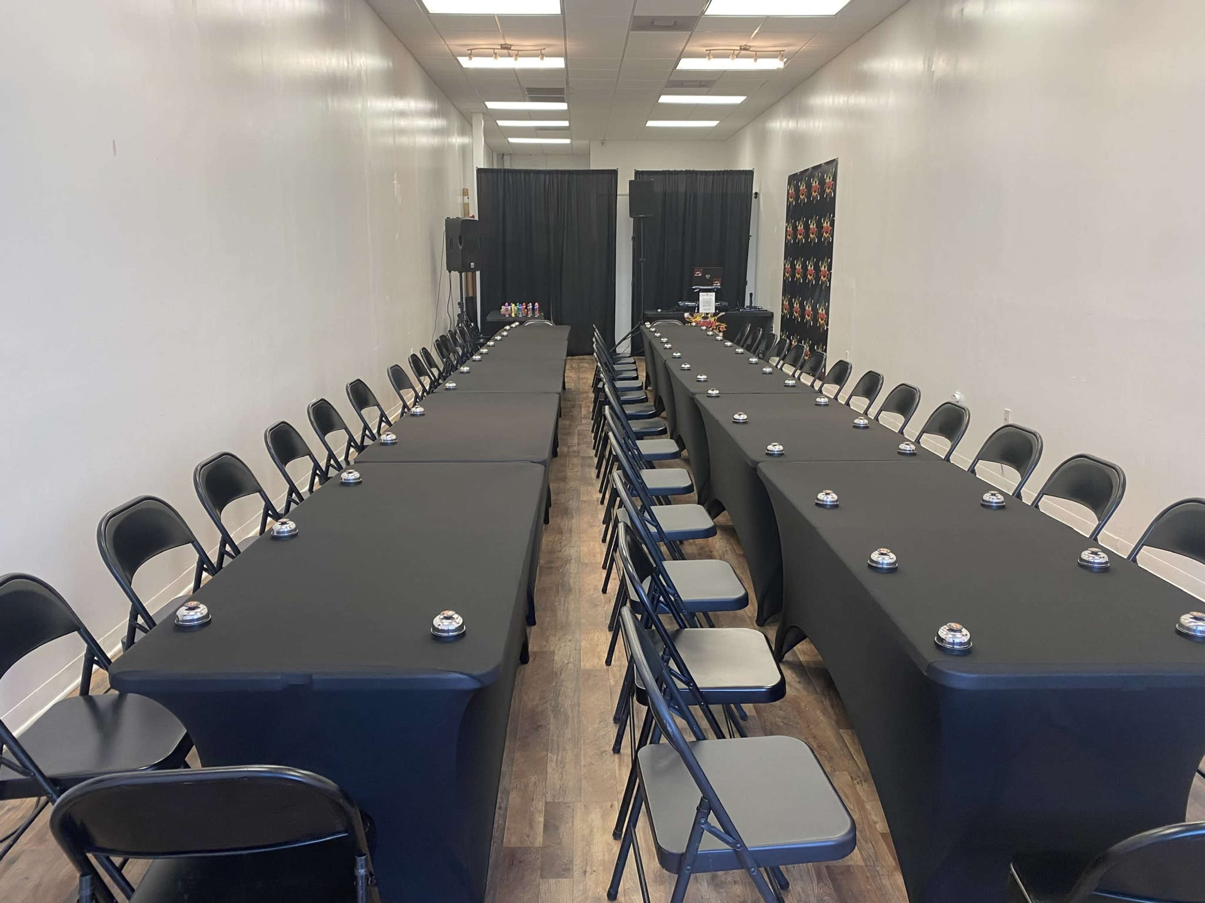 A rectangular conference room setup with two long tables covered in black cloth, facing each other with chairs arranged along both sides.