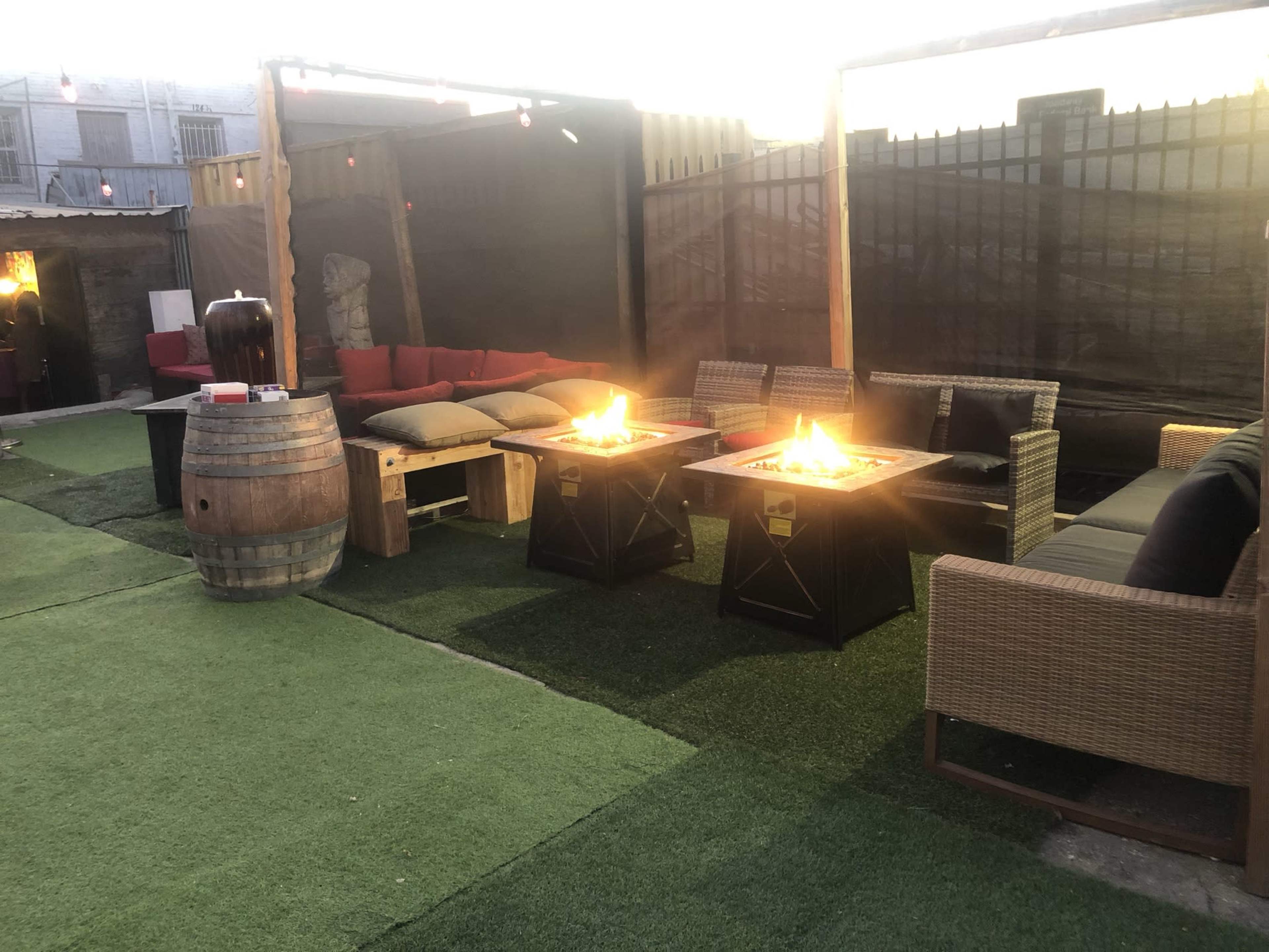 The image shows an outdoor seating area with two fire pits, surrounded by various sofas and a barrel table on a green lawn.