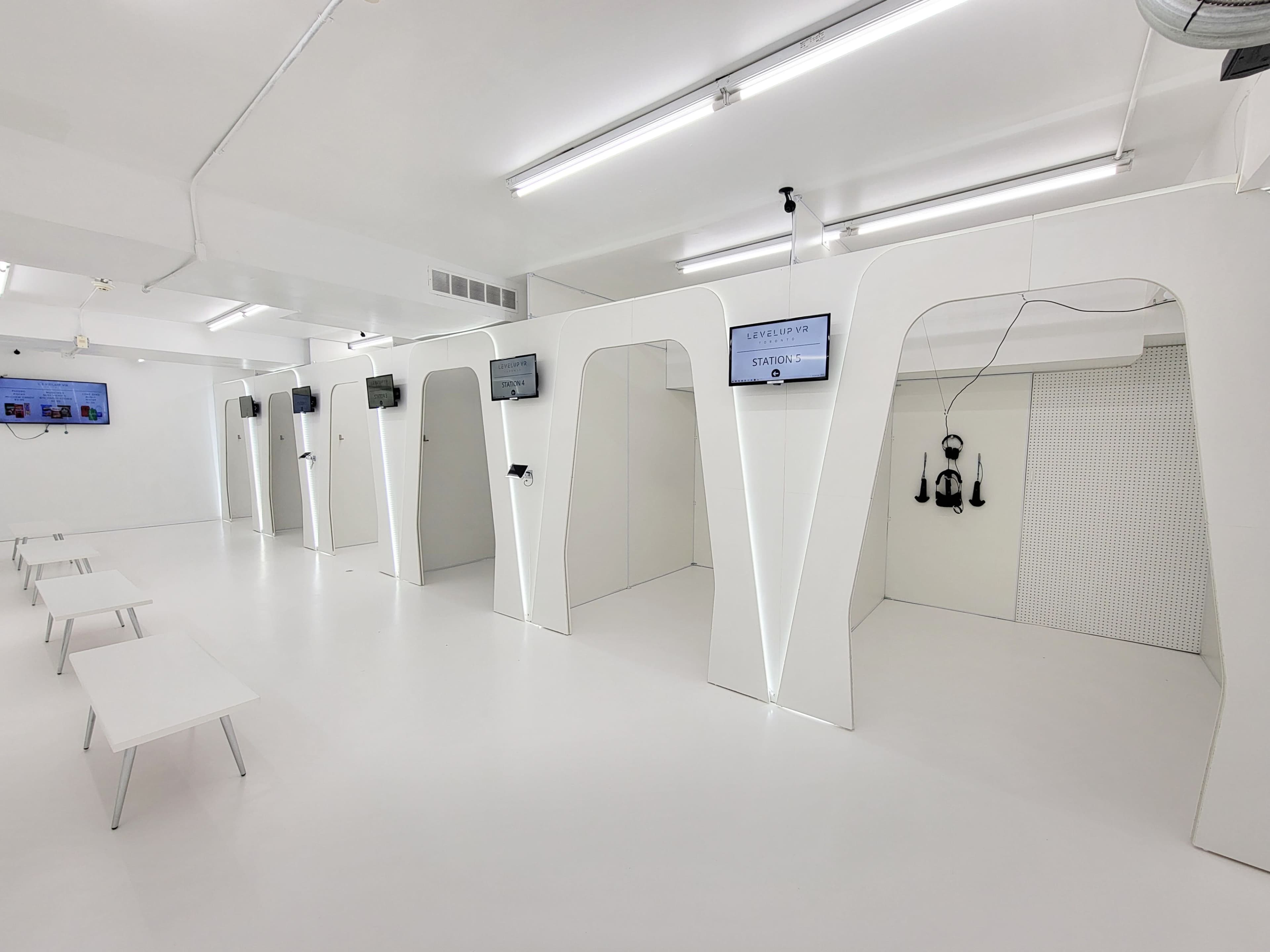 The image shows a modern, minimalist room with several alcoves featuring screens and equipment, designed for technology or virtual reality use.