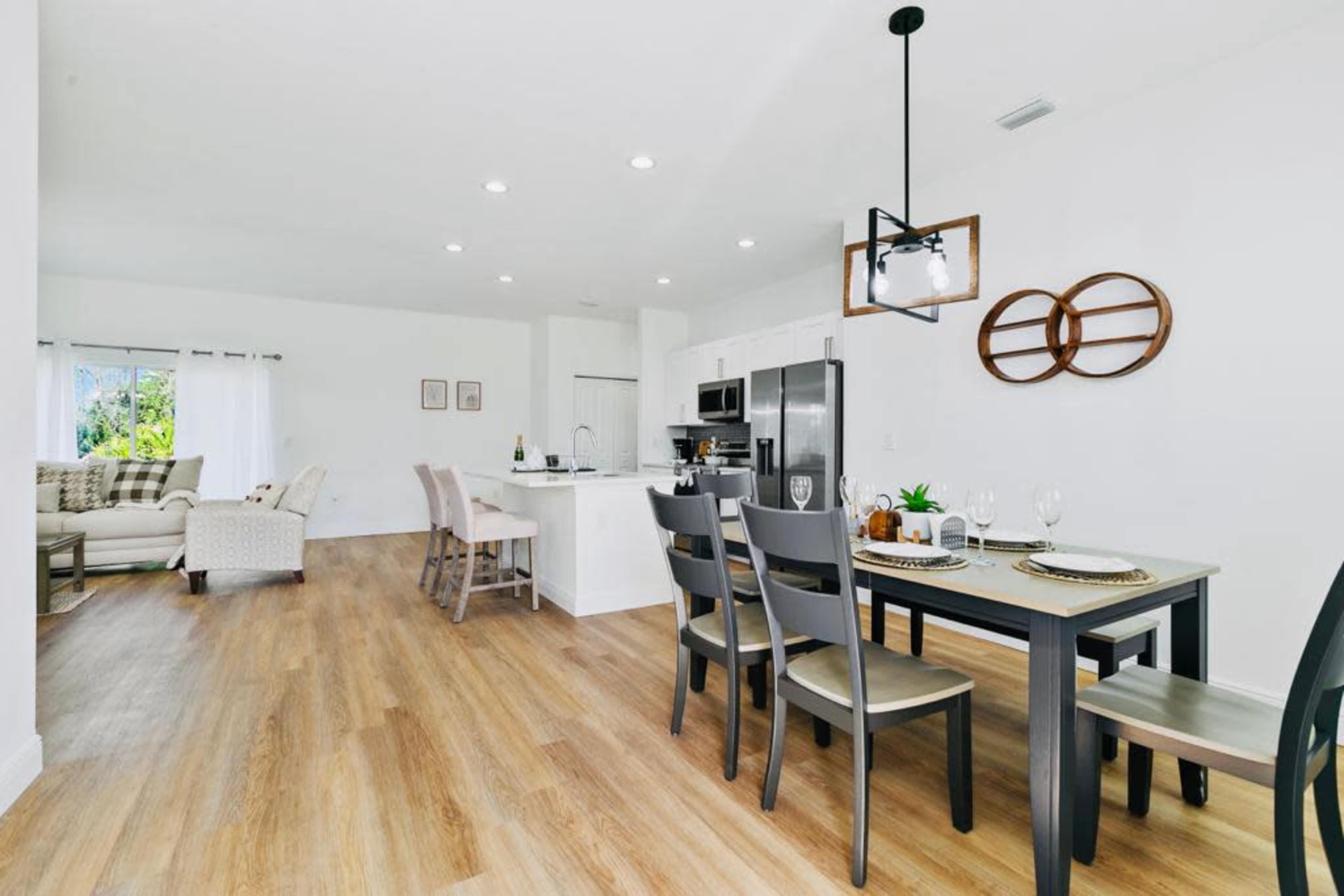 The image shows a modern open-concept living space with a dining area featuring a table set for meals and a cozy seating area in the background.