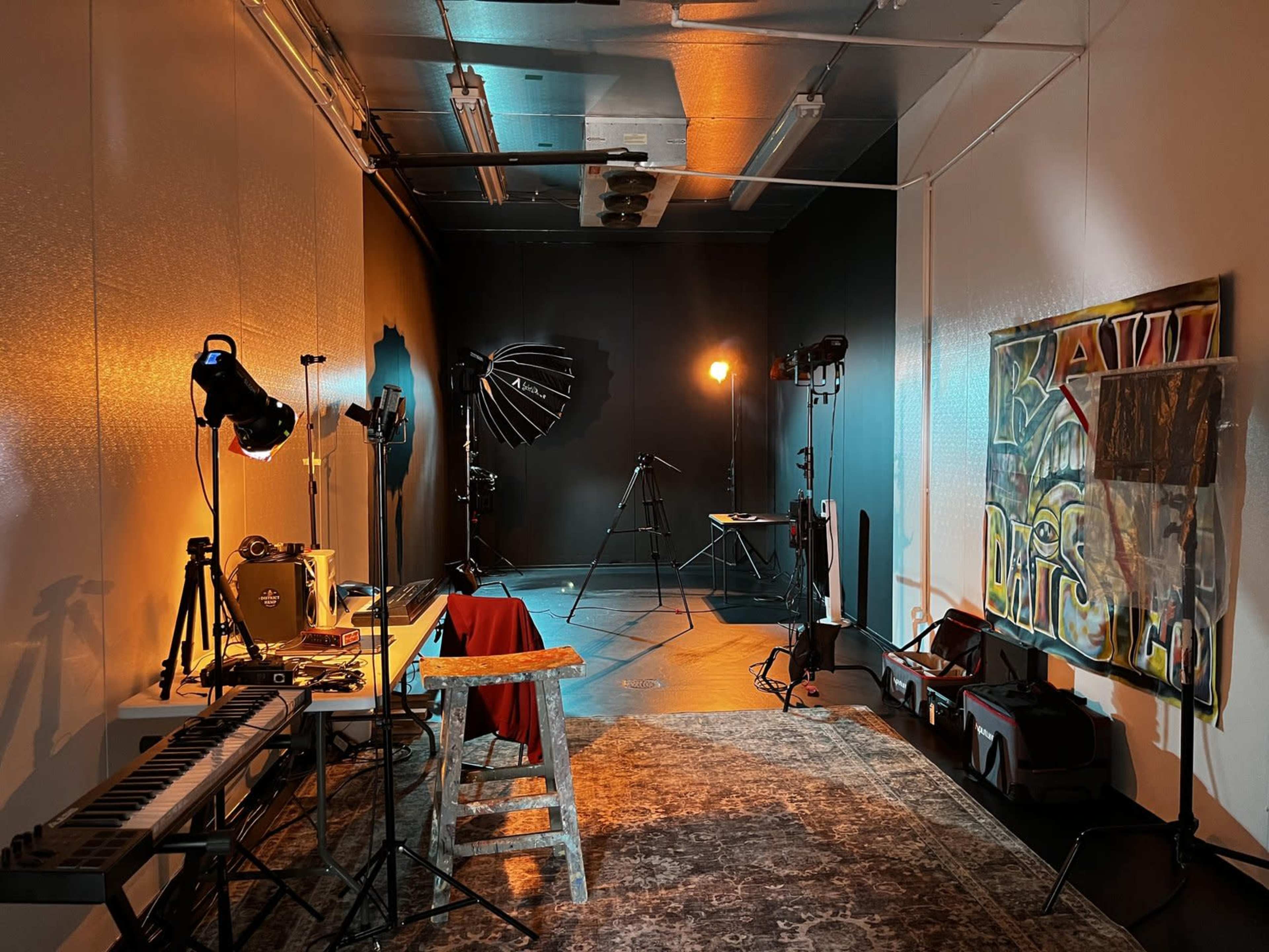The image shows a studio space equipped with various lighting setups, musical instruments, and a large backdrop painting on one wall.