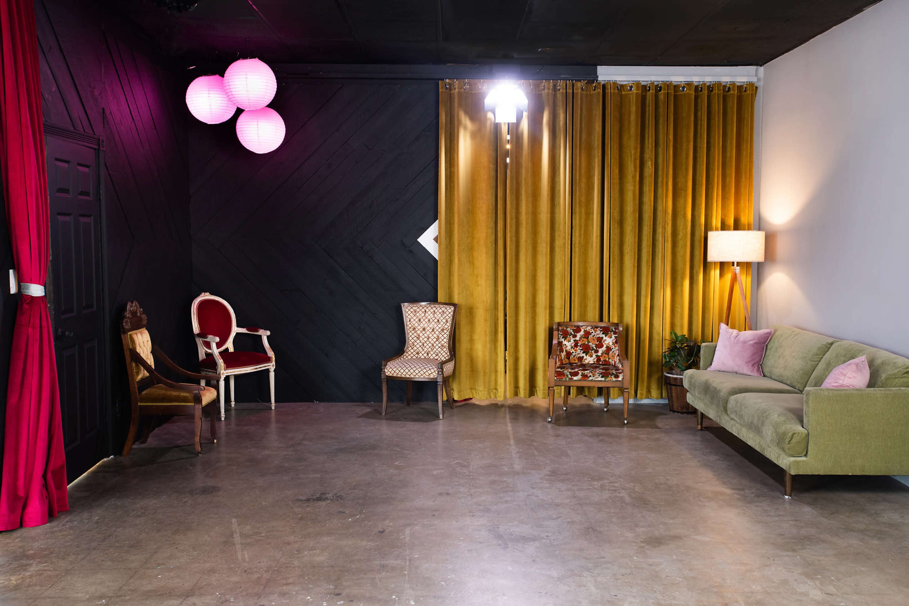The image shows a room with a concrete floor, black and yellow walls, several chairs, a green sofa, and decorative lighting.