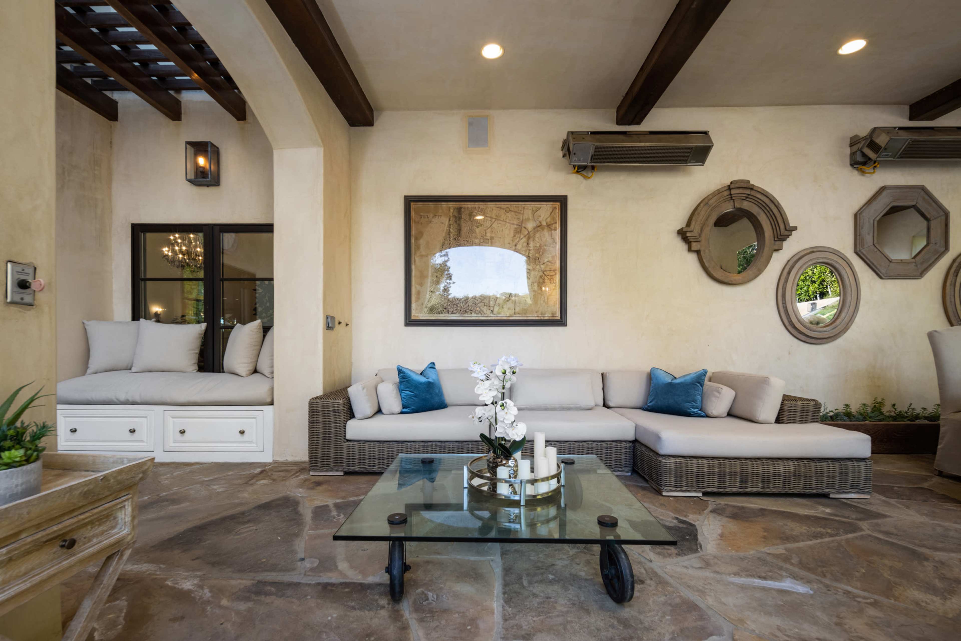 The image shows a stylish living room with a large sectional sofa, a glass coffee table, and decorative mirrors on the walls.
