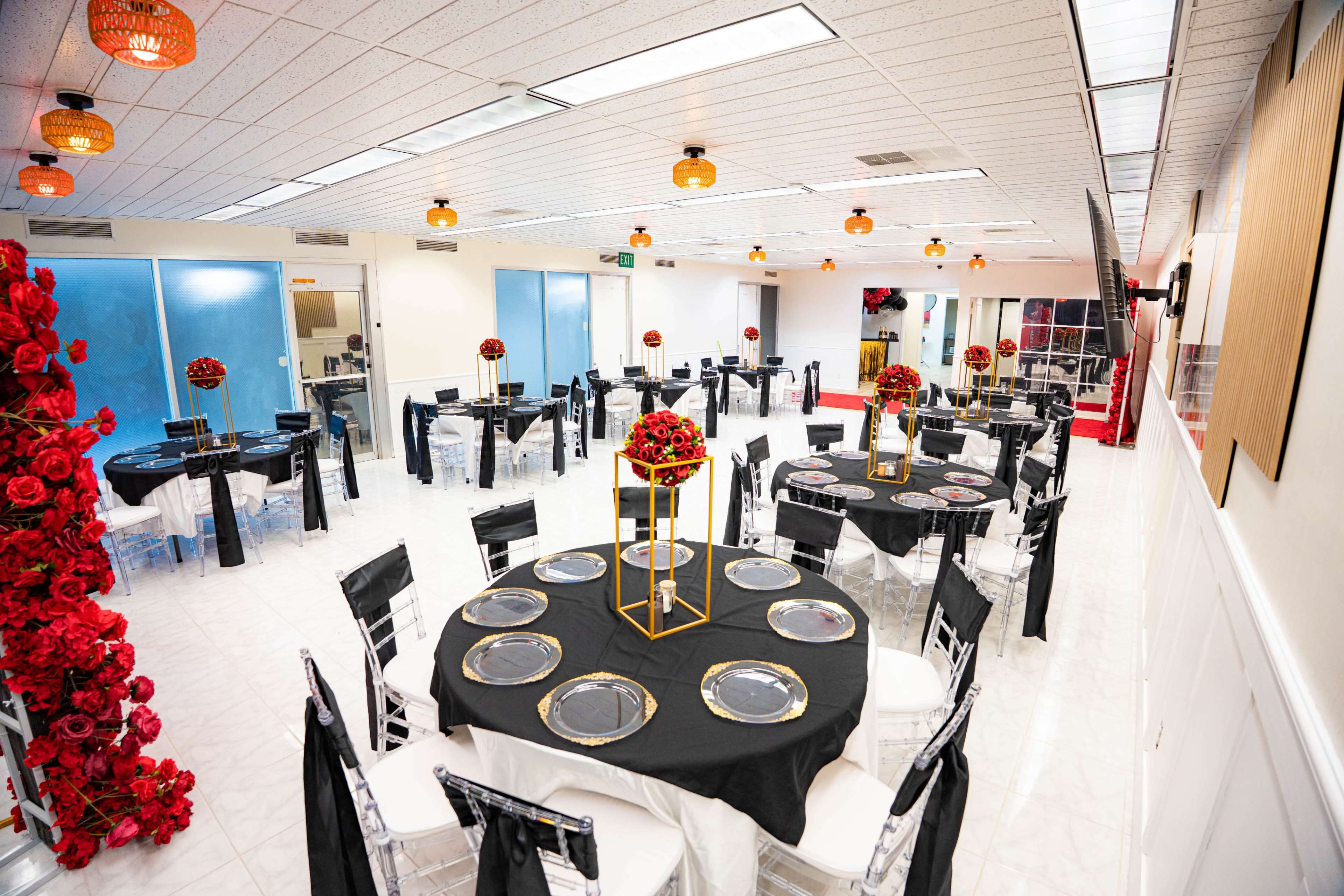The image shows an elegantly arranged banquet hall featuring several round tables dressed in black tablecloths, each adorned with floral centerpieces, surrounded by clear acrylic chairs.