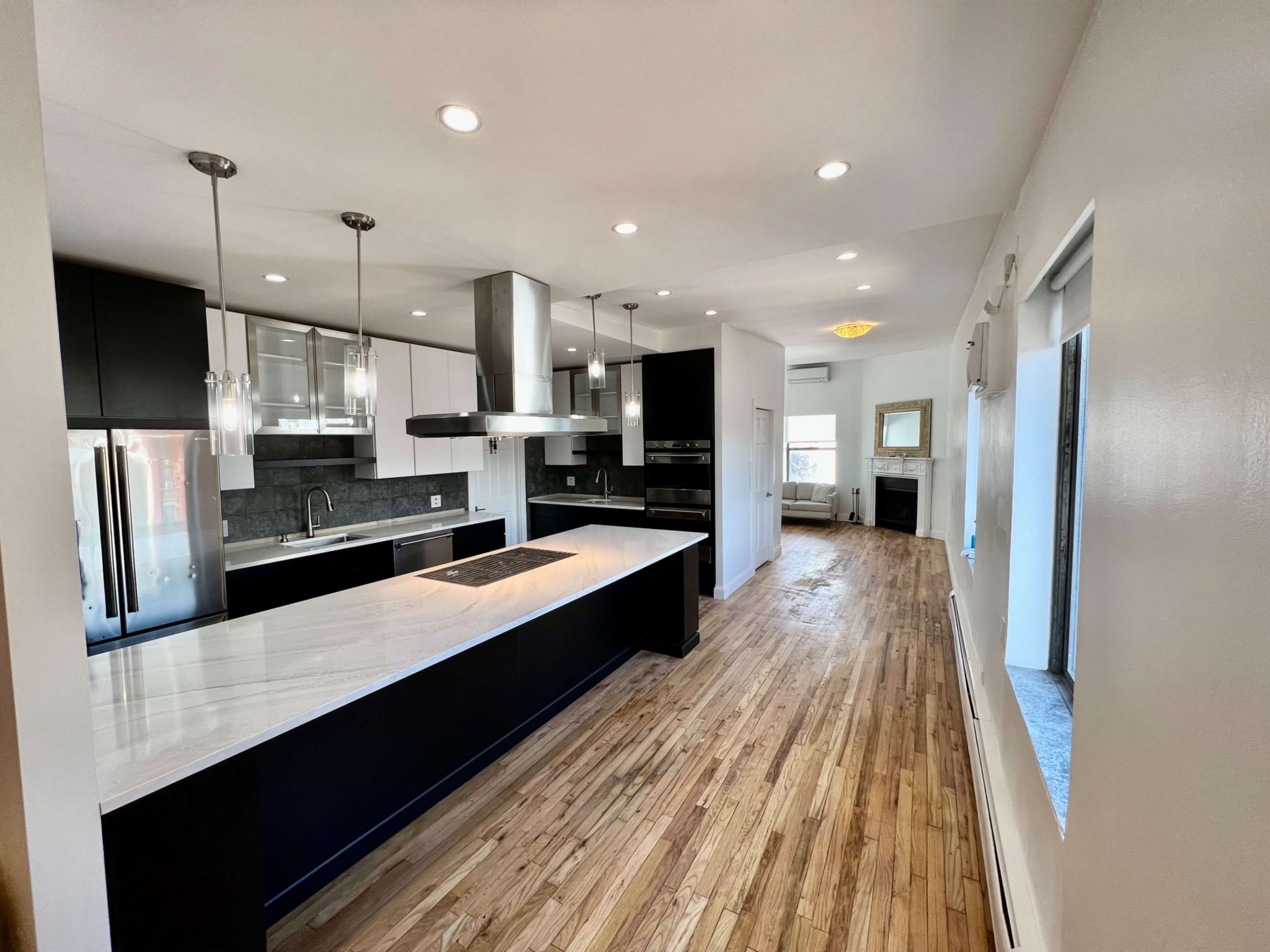 The image shows a modern kitchen with black and white cabinetry, a central island, pendant lighting, and hardwood flooring.