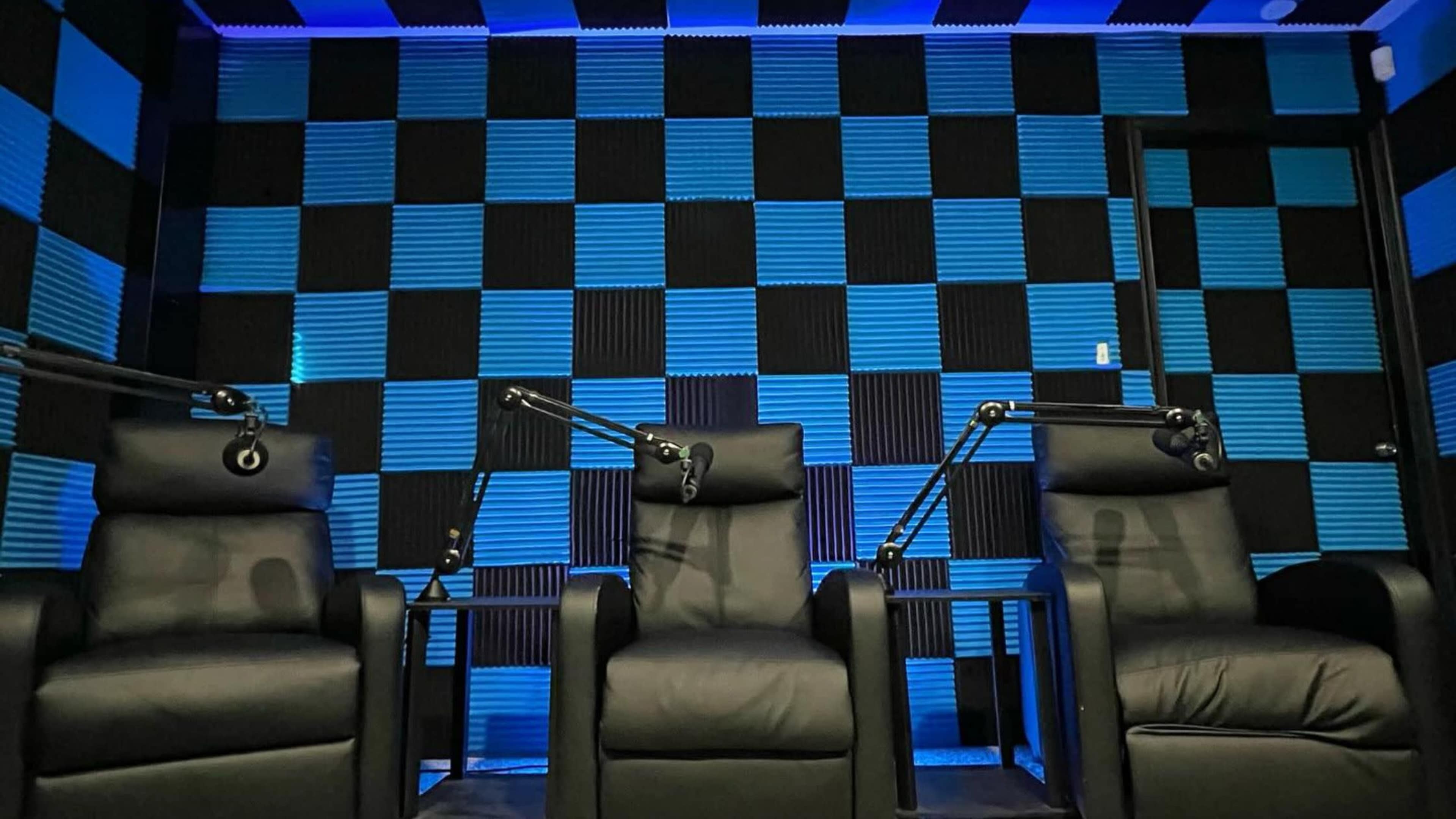 Three black chairs with adjustable arms positioned in front of a blue and black checkered soundproof wall.