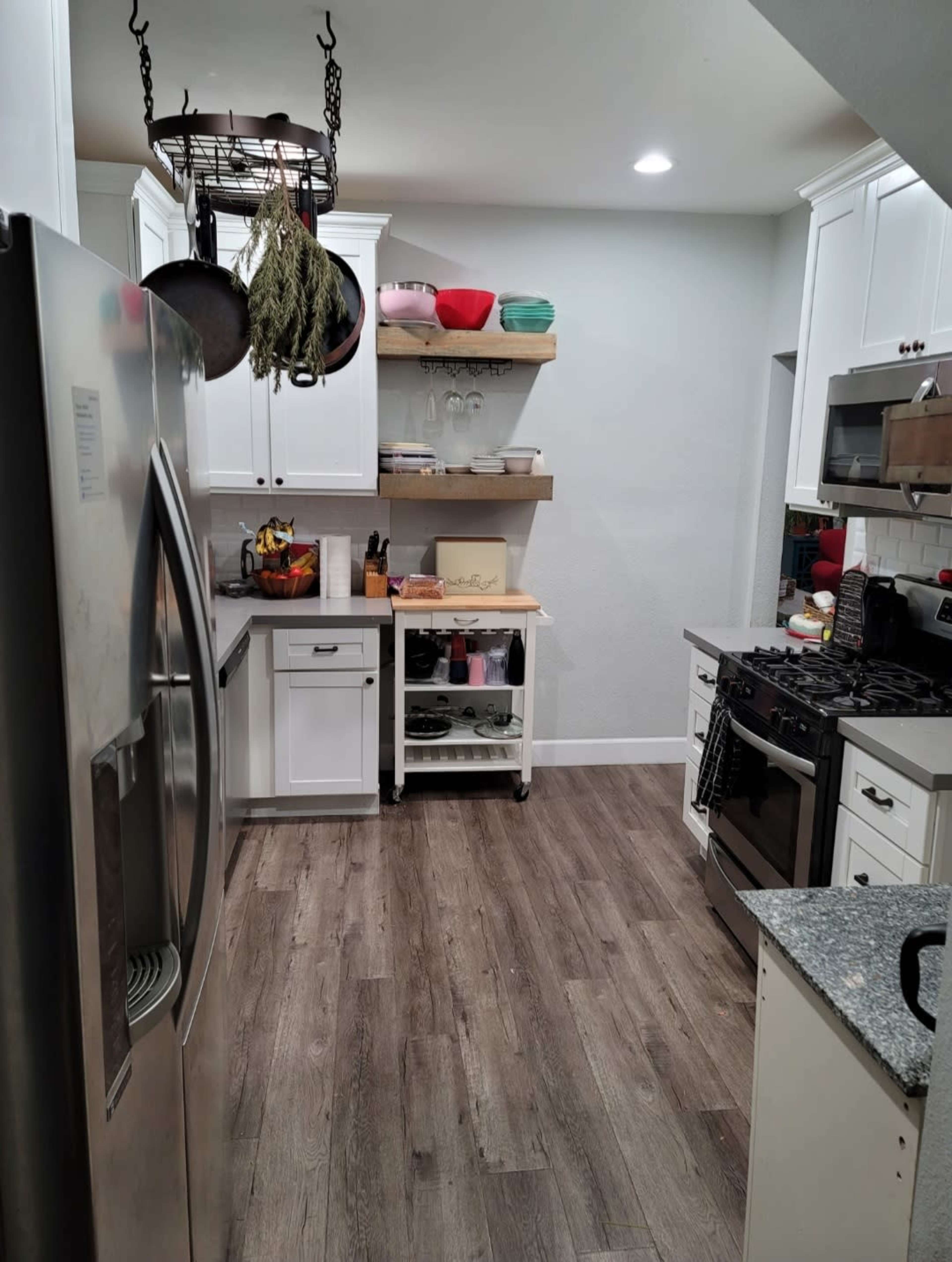 A kitchen features stainless steel appliances, gray countertops, white cabinets, and open shelving with various bowls and utensils.