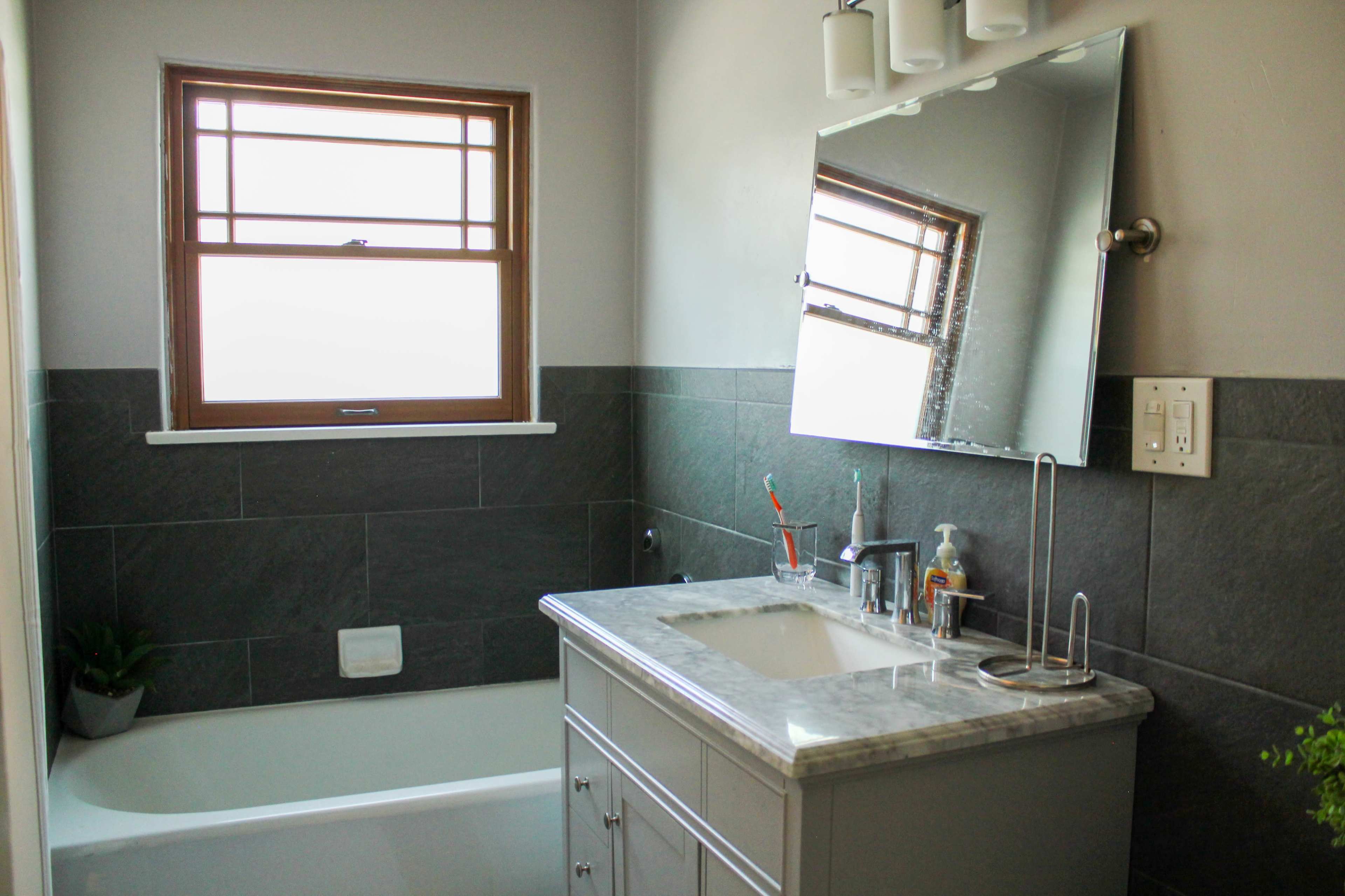 The image shows a modern bathroom with a bathtub, a vanity with a sink, and a large mirror above it.