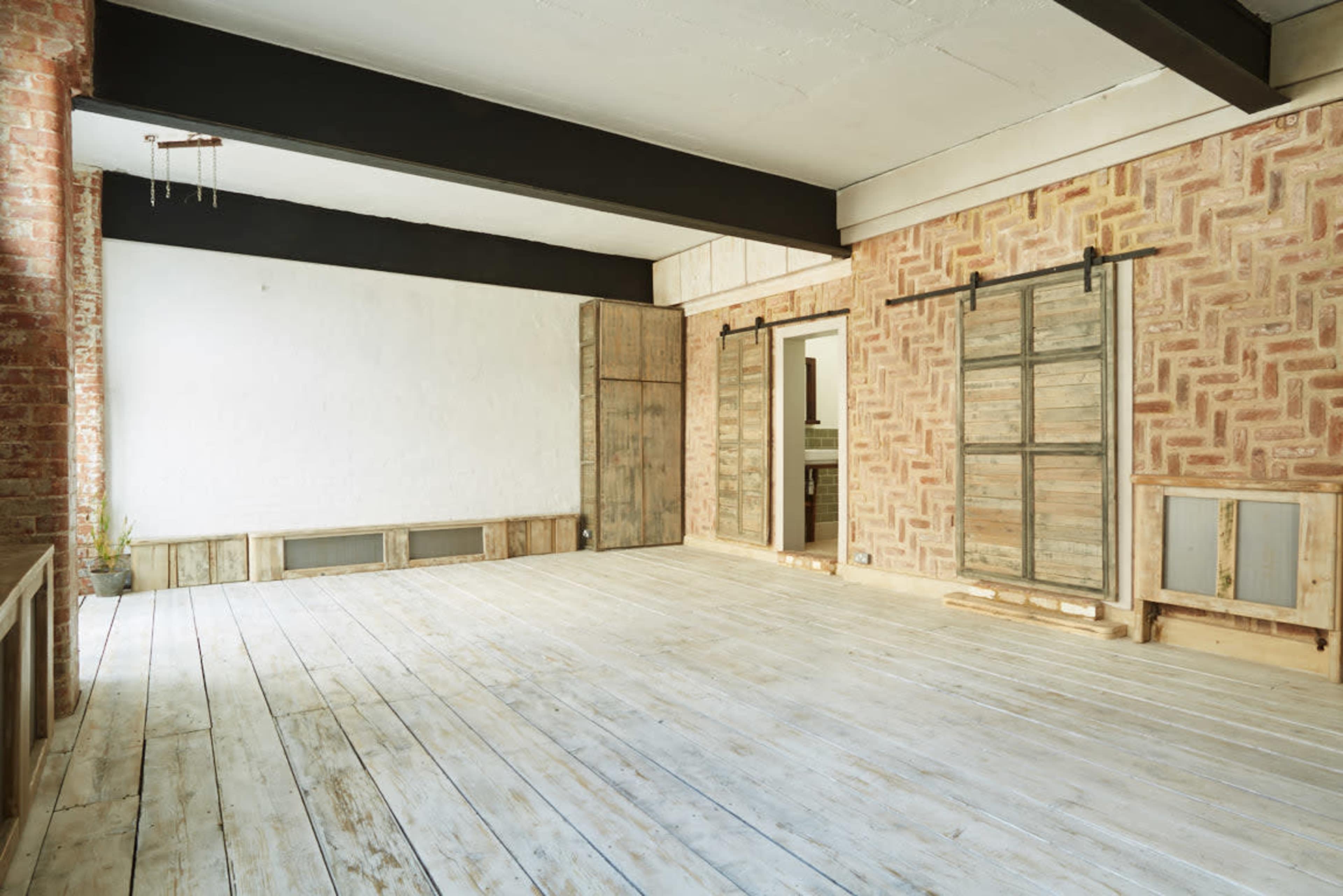 An empty room with wooden floors and walls featuring a textured brick and patterned design.